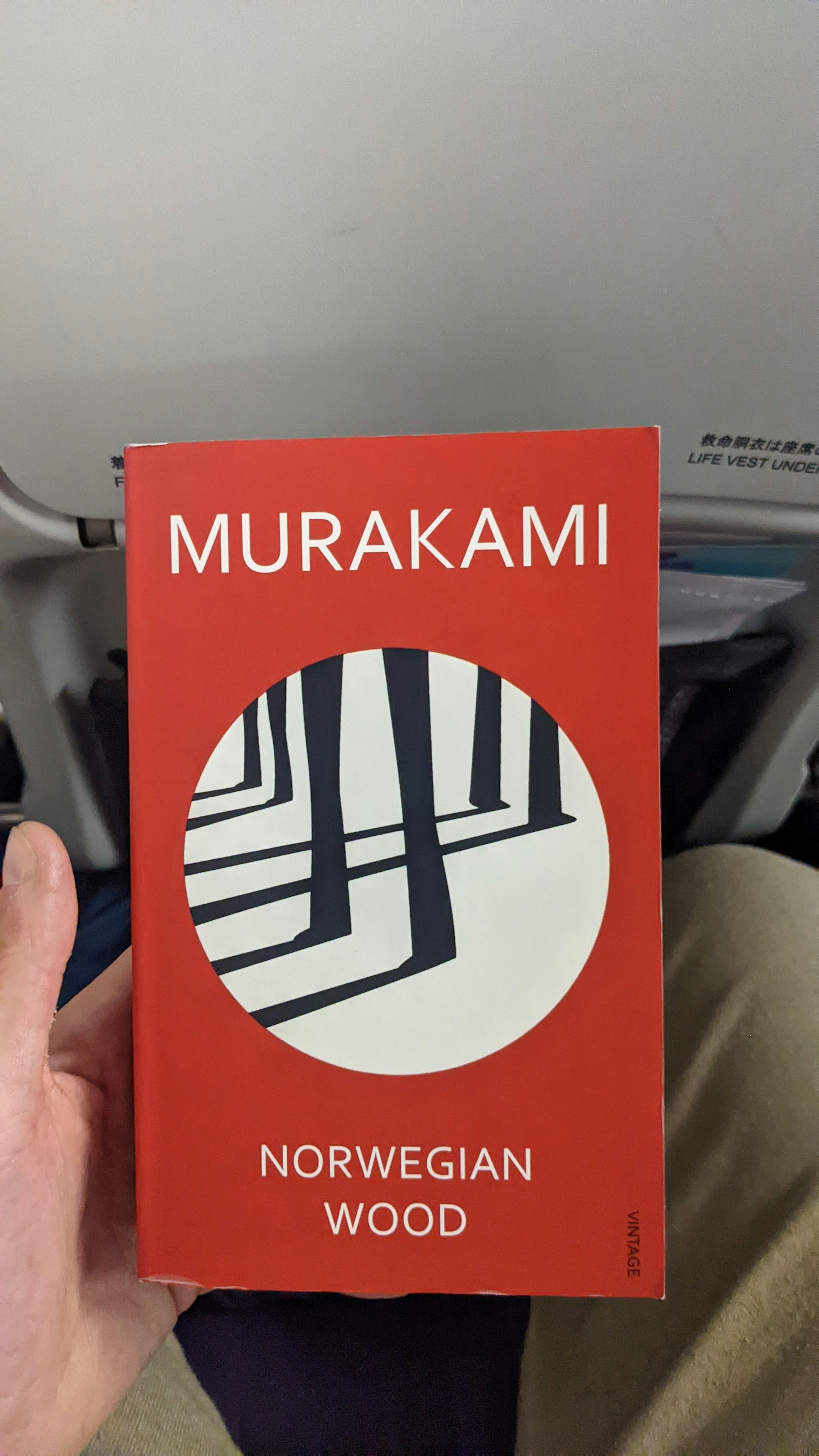 Sebuah tangan memegang sampul buku Norwegian Wood karya Murakami