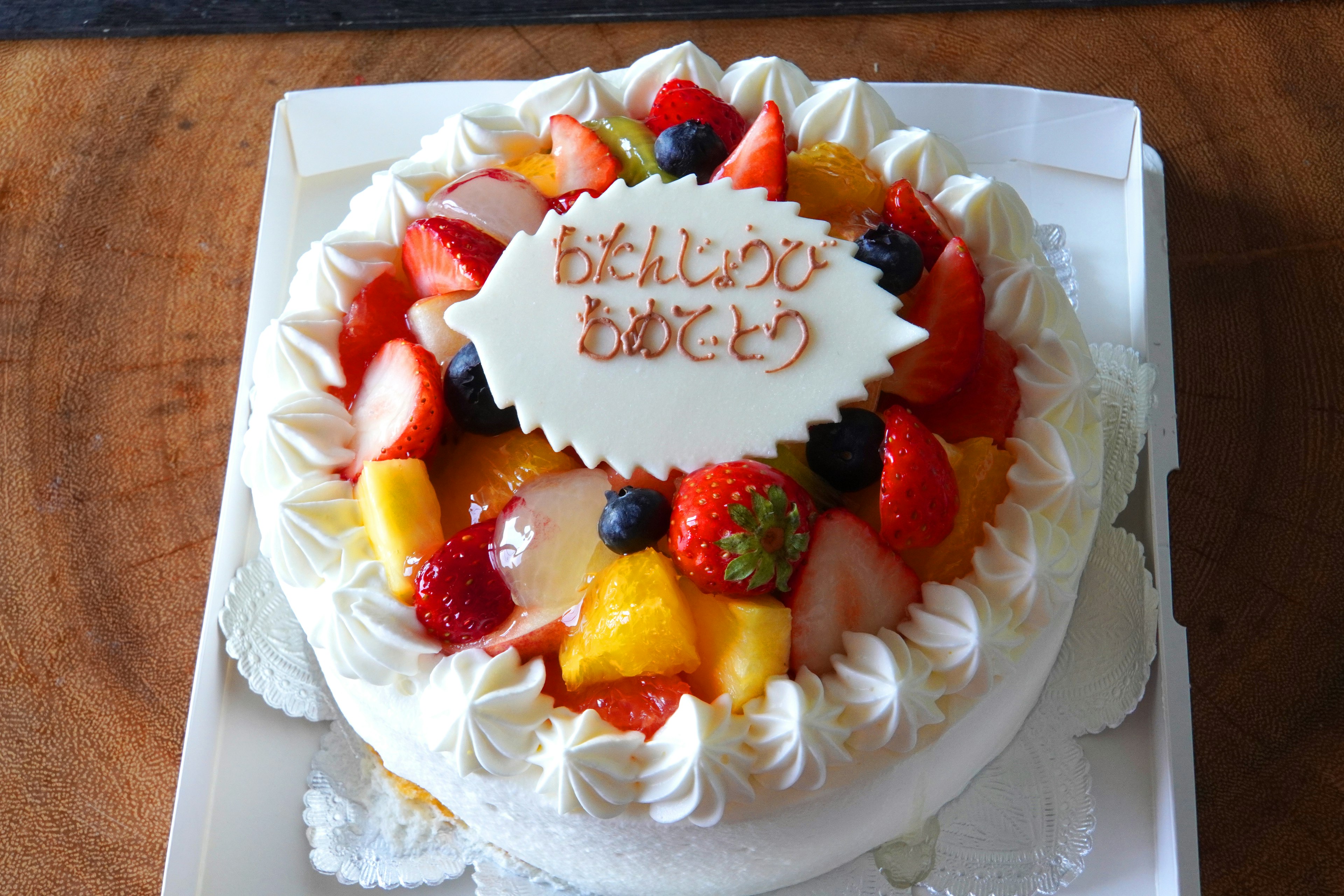 Fruit-topped white cream cake with a birthday message