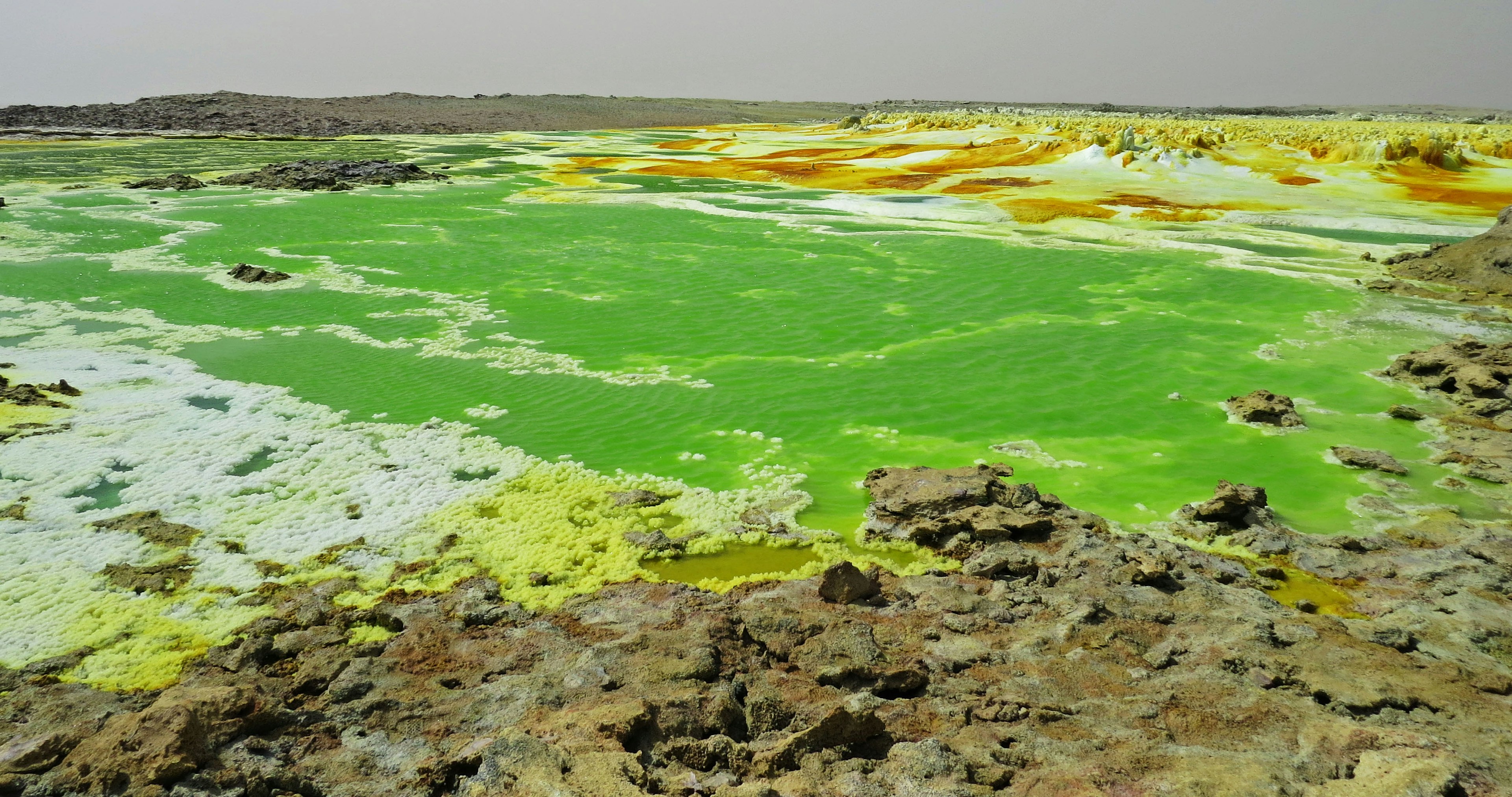 Lago verde vibrante con formazioni minerali gialle in un paesaggio unico