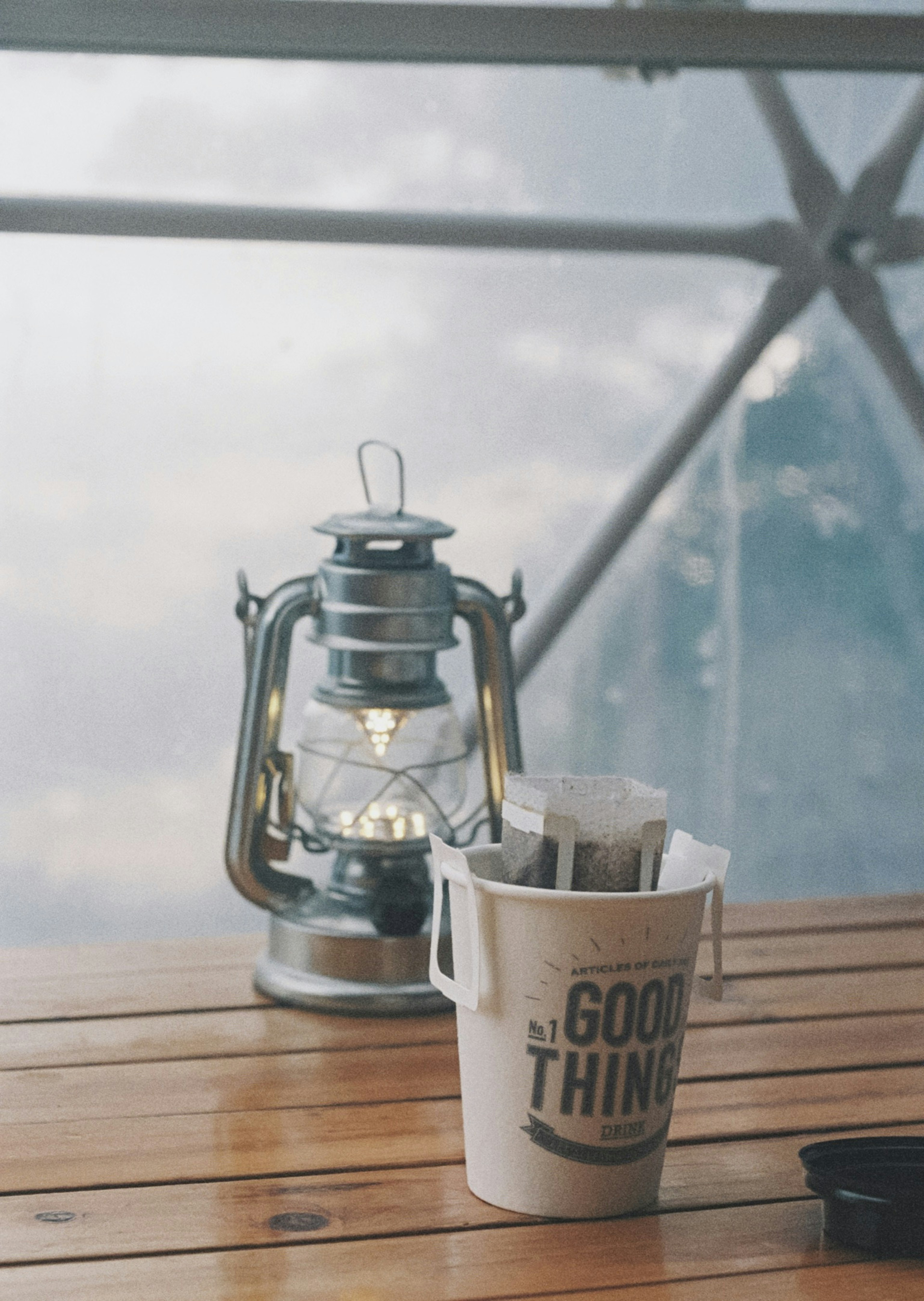 Silver lantern on a wooden table with a bucket labeled GOOD THINGS