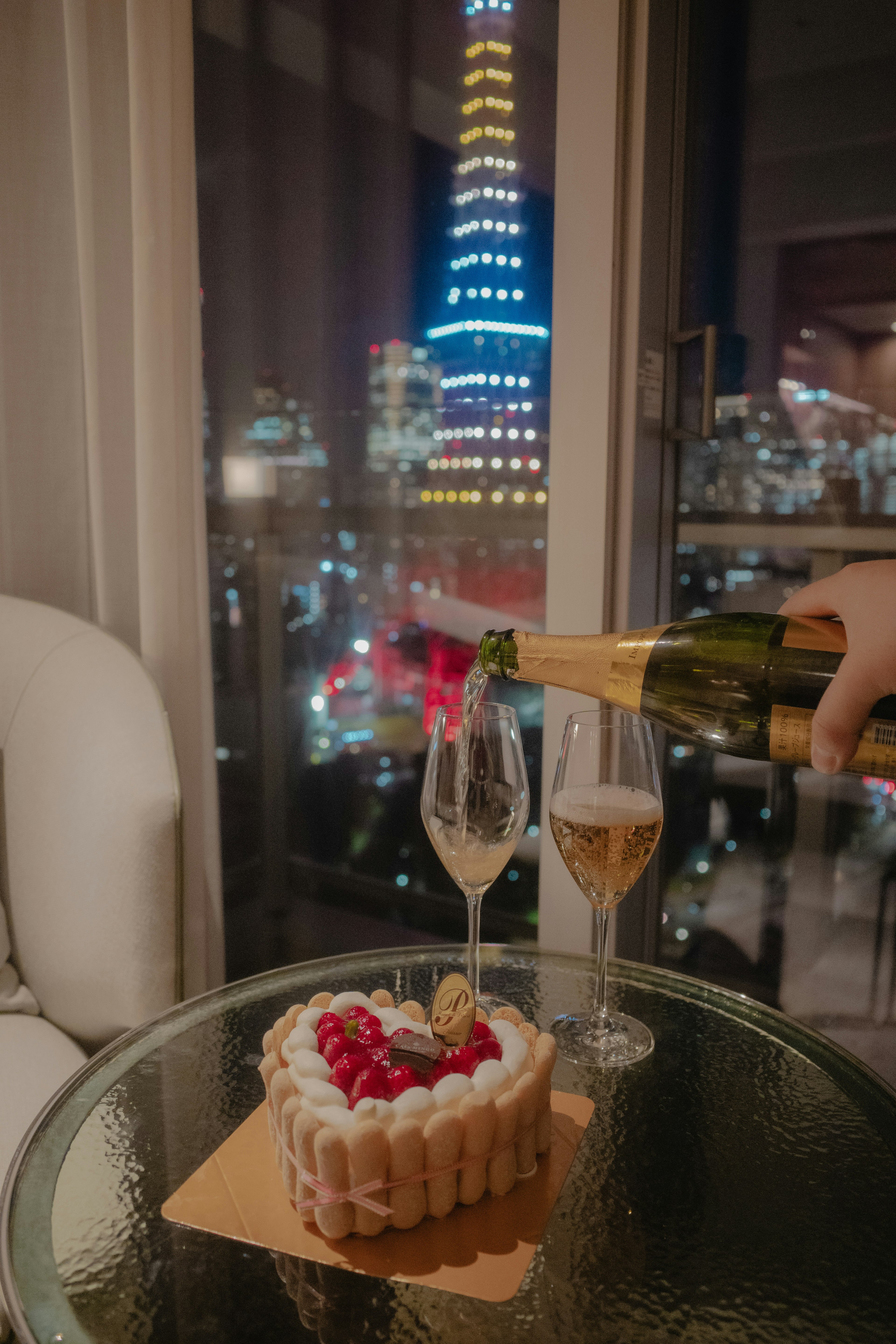 Mesa con champán y pastel con vista nocturna de la ciudad