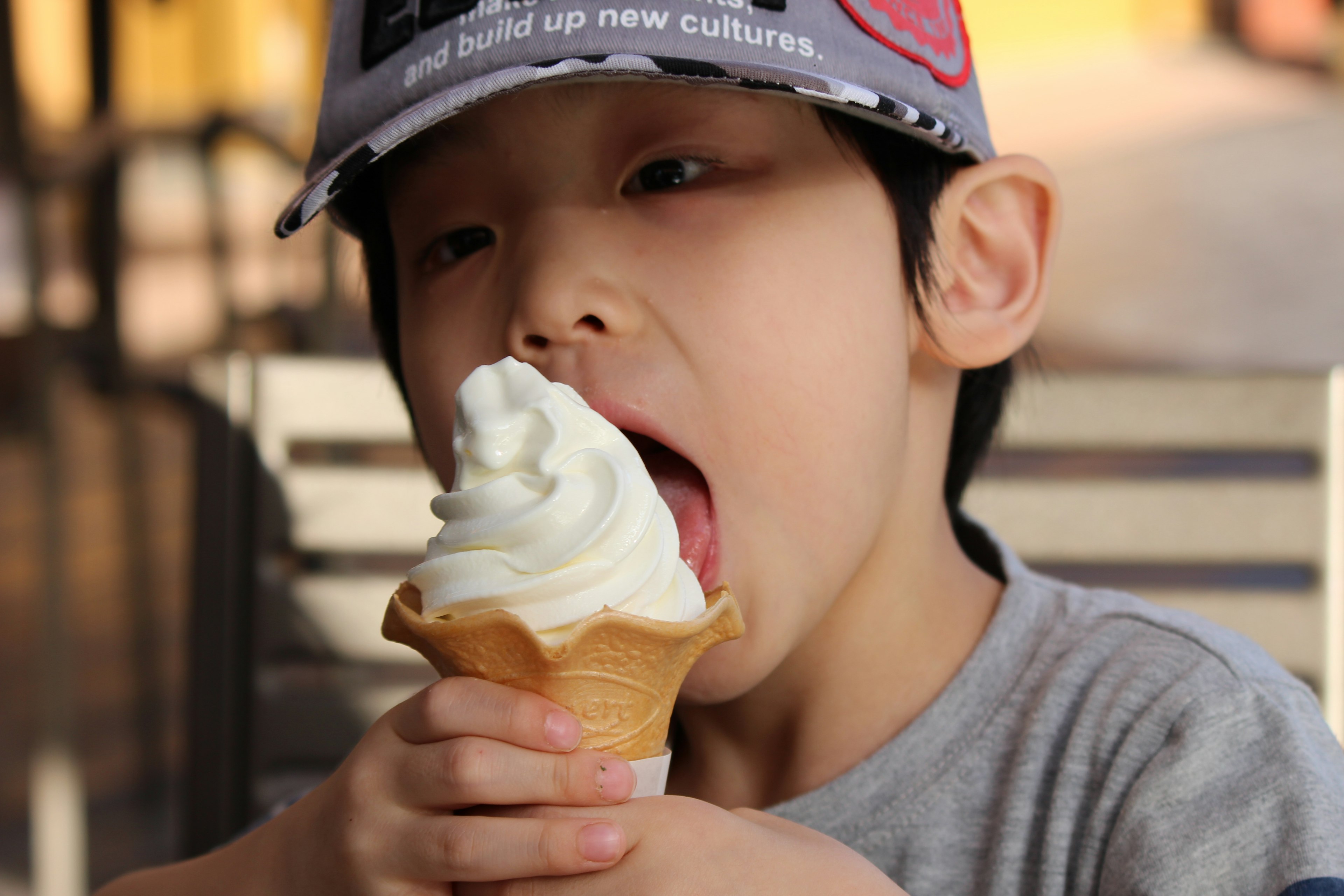 アイスクリームを食べる子供の写真帽子をかぶった少年がソフトクリームを舌でなめている