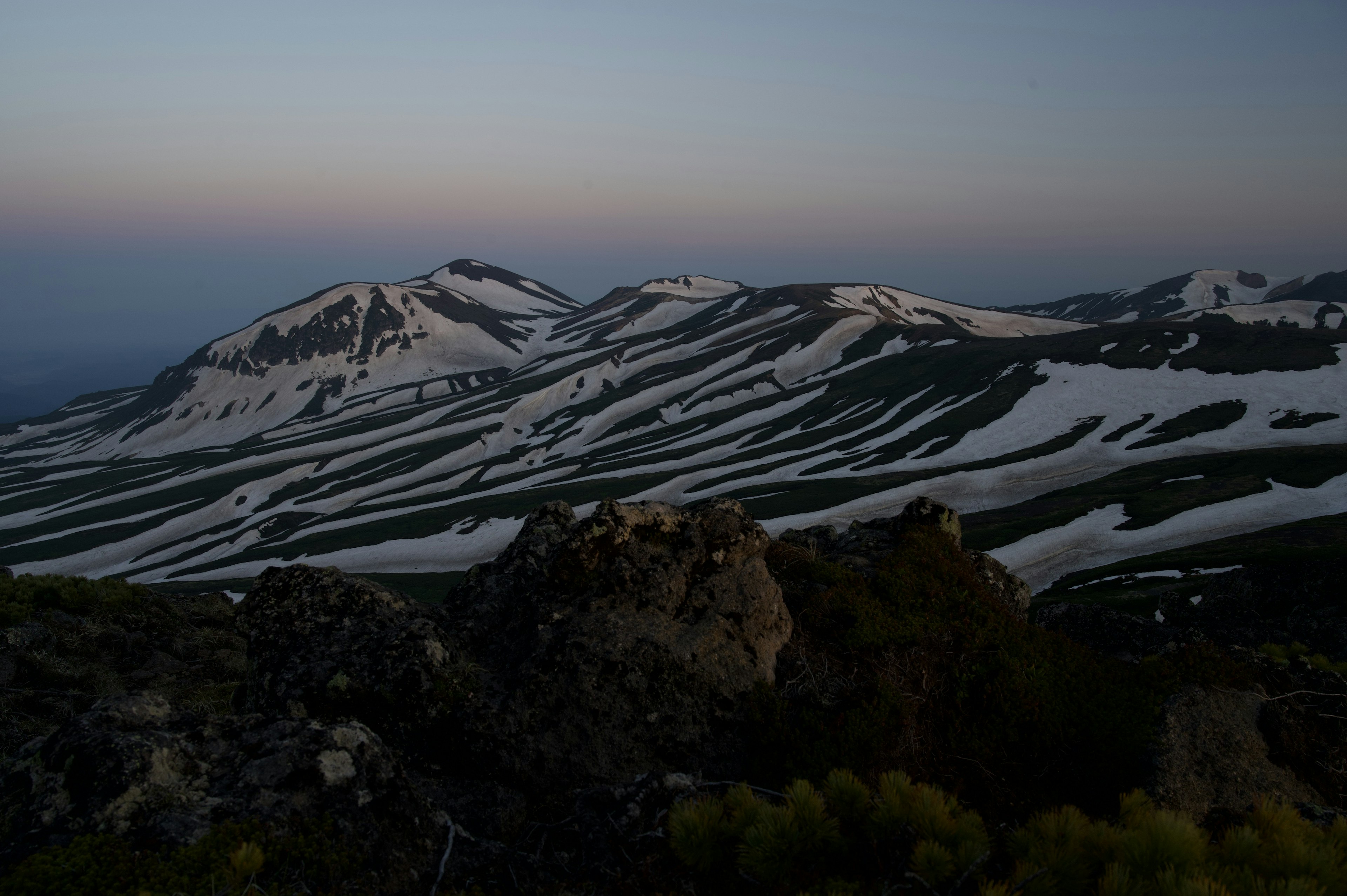 Montagnes enneigées avec des pentes vertes au crépuscule