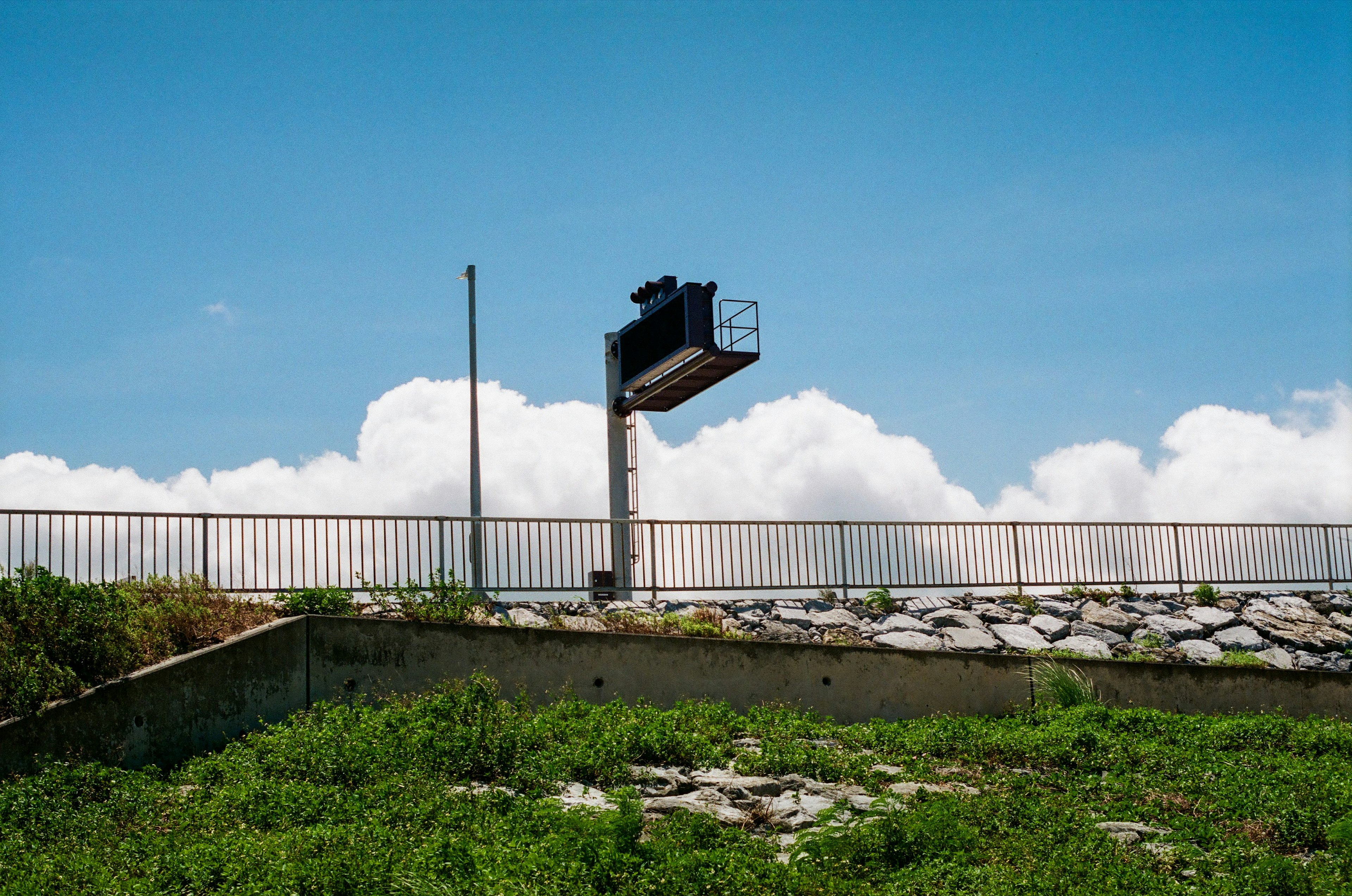 Schwarzes Schild unter einem blauen Himmel mit weißen Wolken und grünem Gras