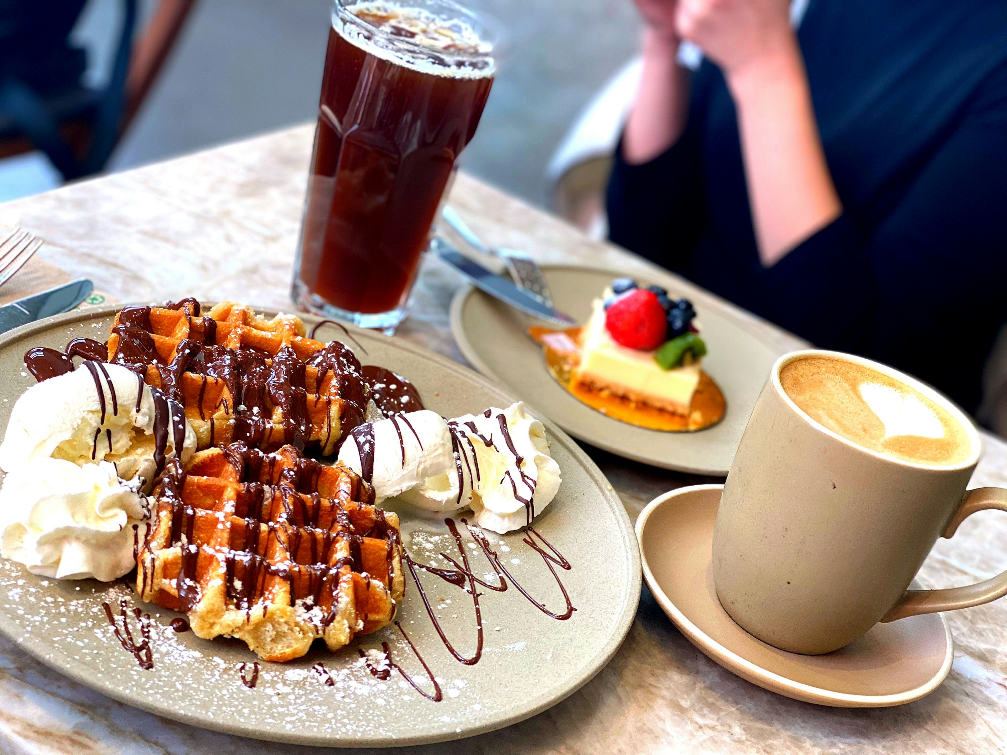 Plato delicioso de waffles con crema batida y chocolate acompañado de café y té helado