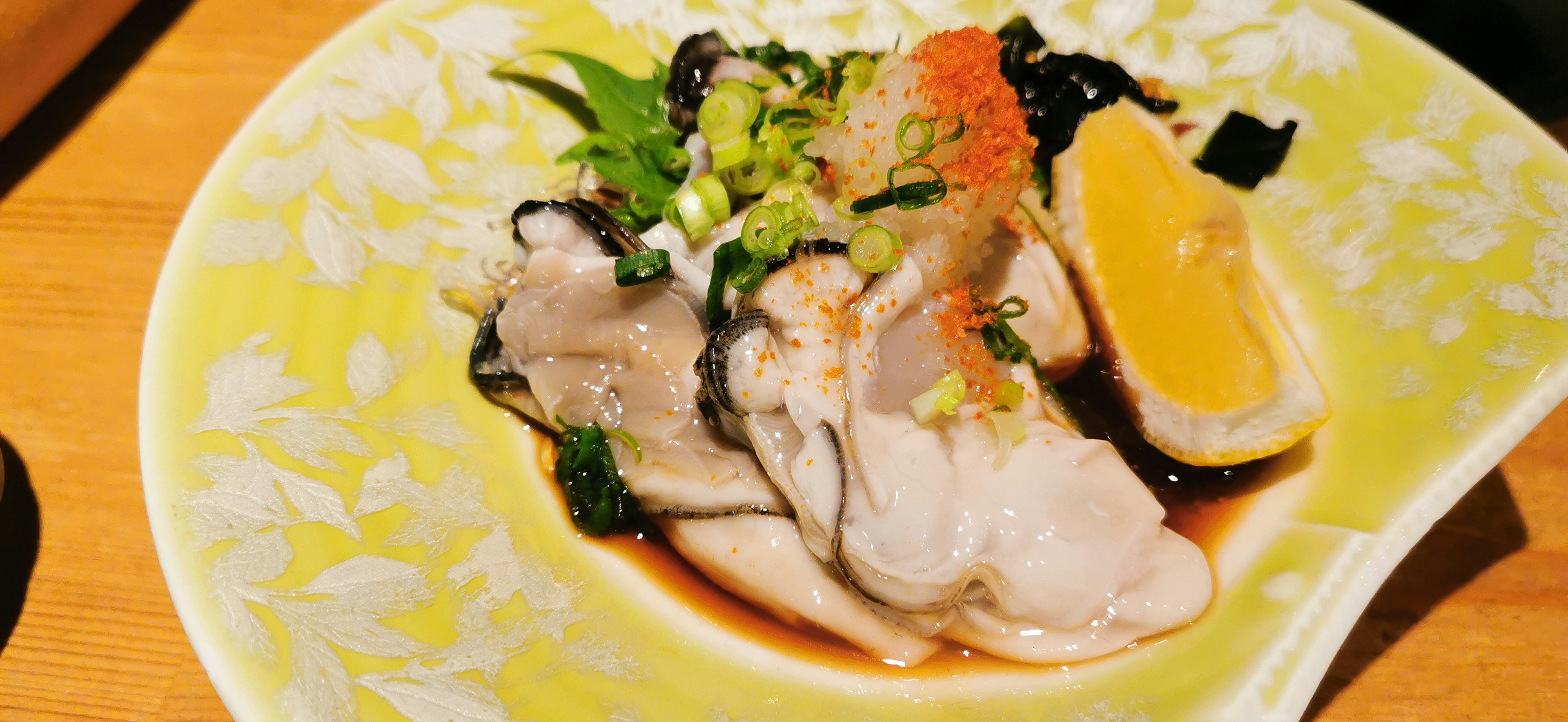 Fresh oysters topped with lemon and scallions on a decorative plate