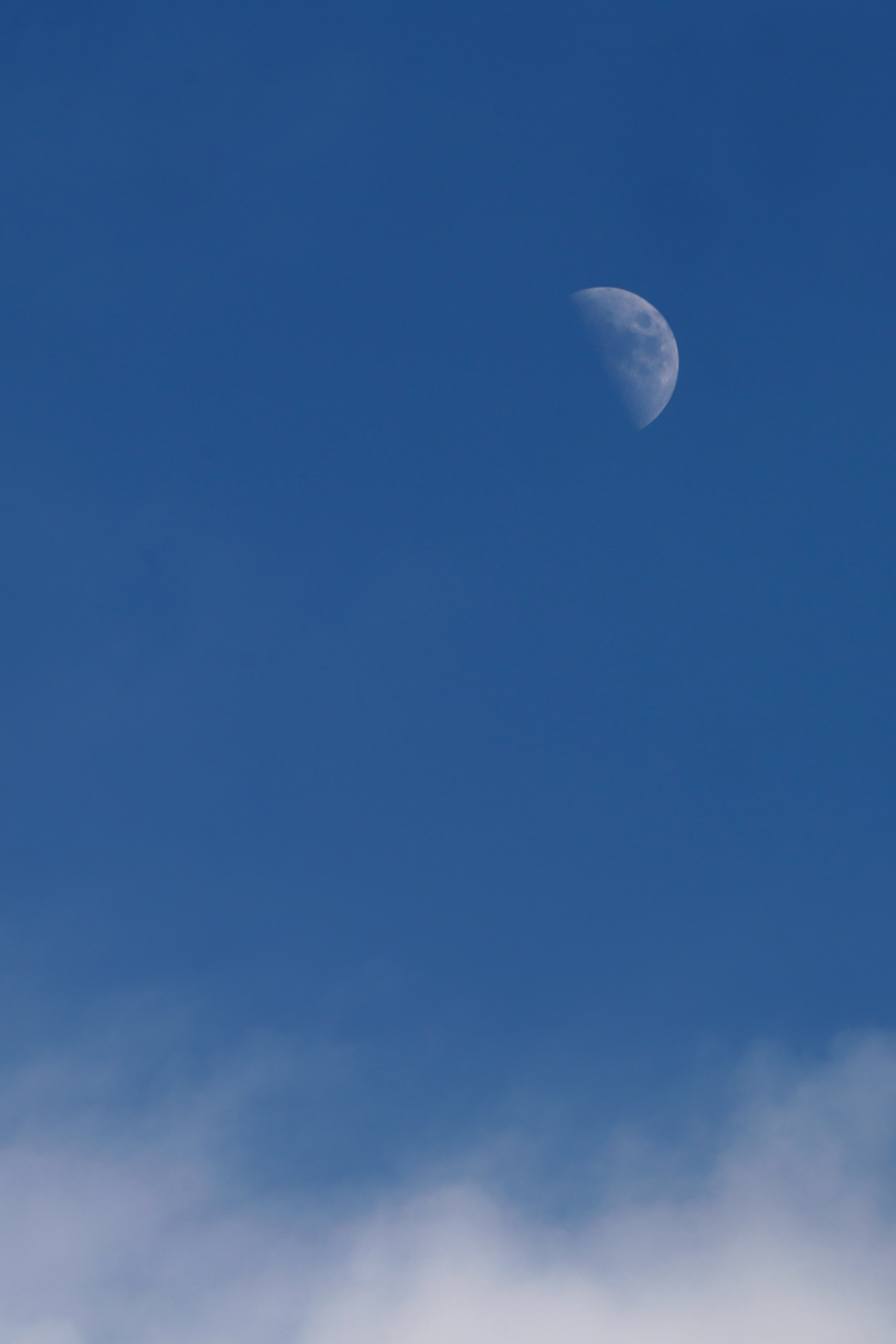 Half moon visible in a clear blue sky with clouds