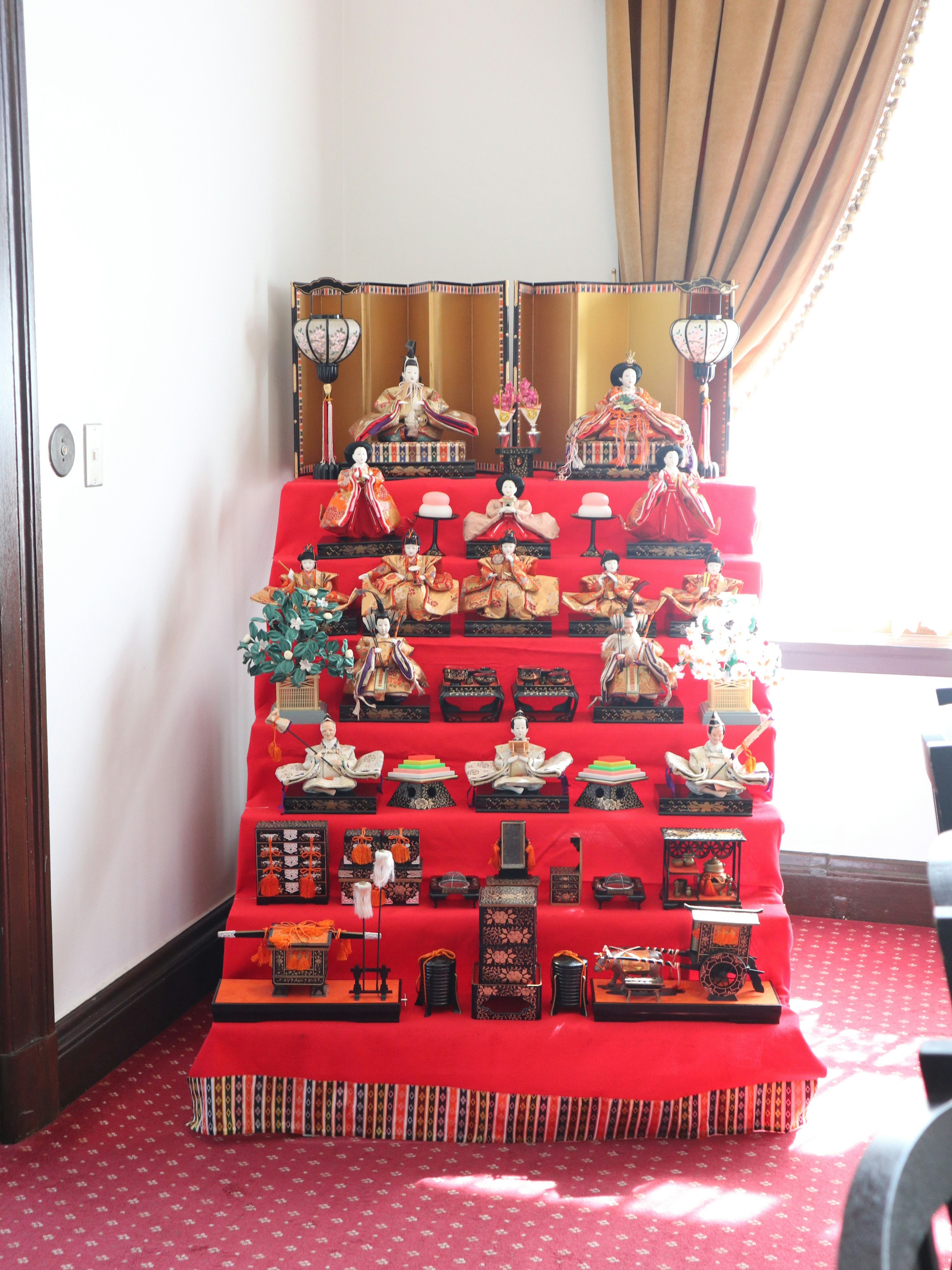 Exhibición de muñecas hina sobre tela roja con una cortina de fondo