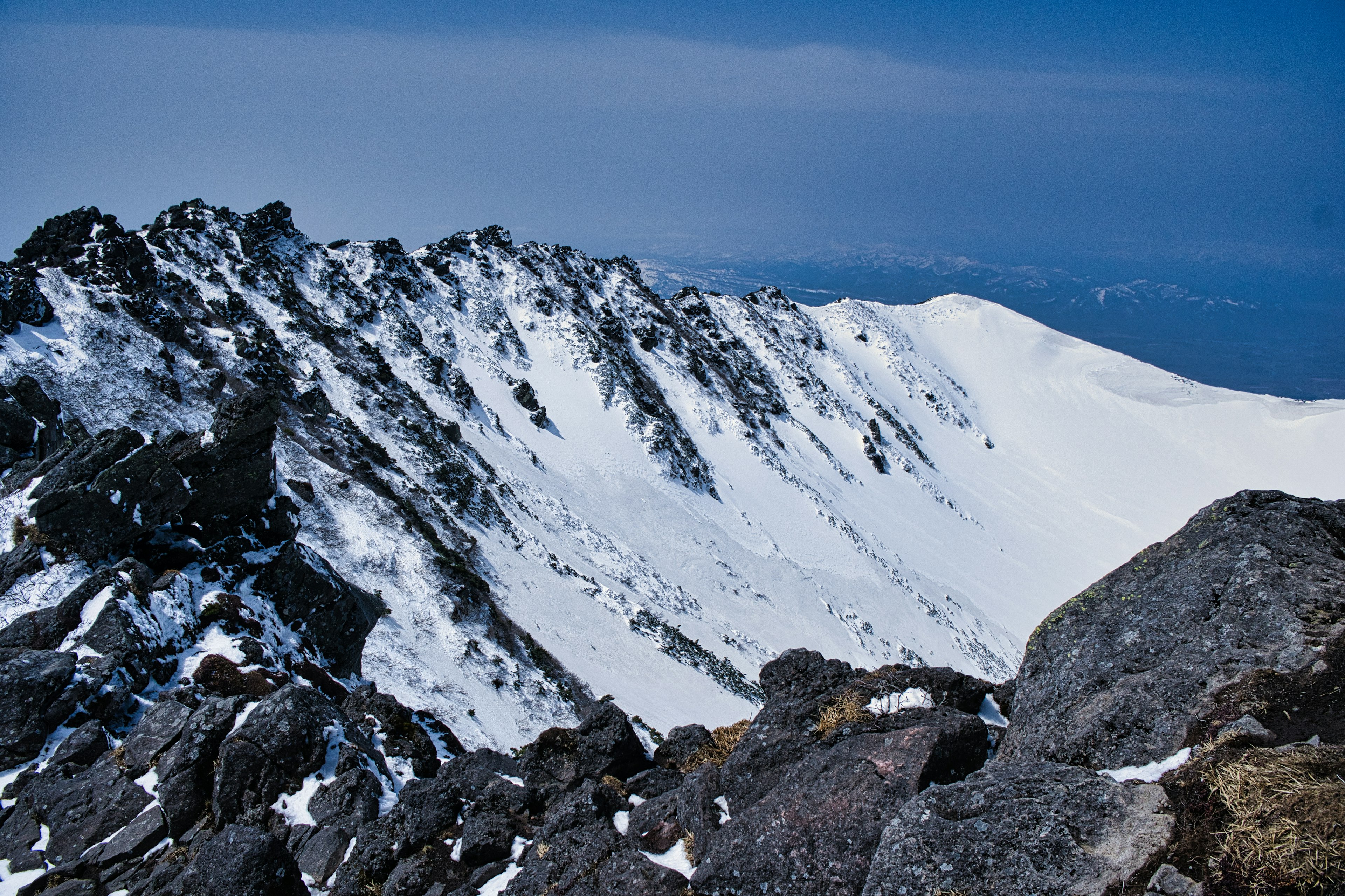 Stunning view of snow-covered mountain range with scattered rocks and clear blue sky