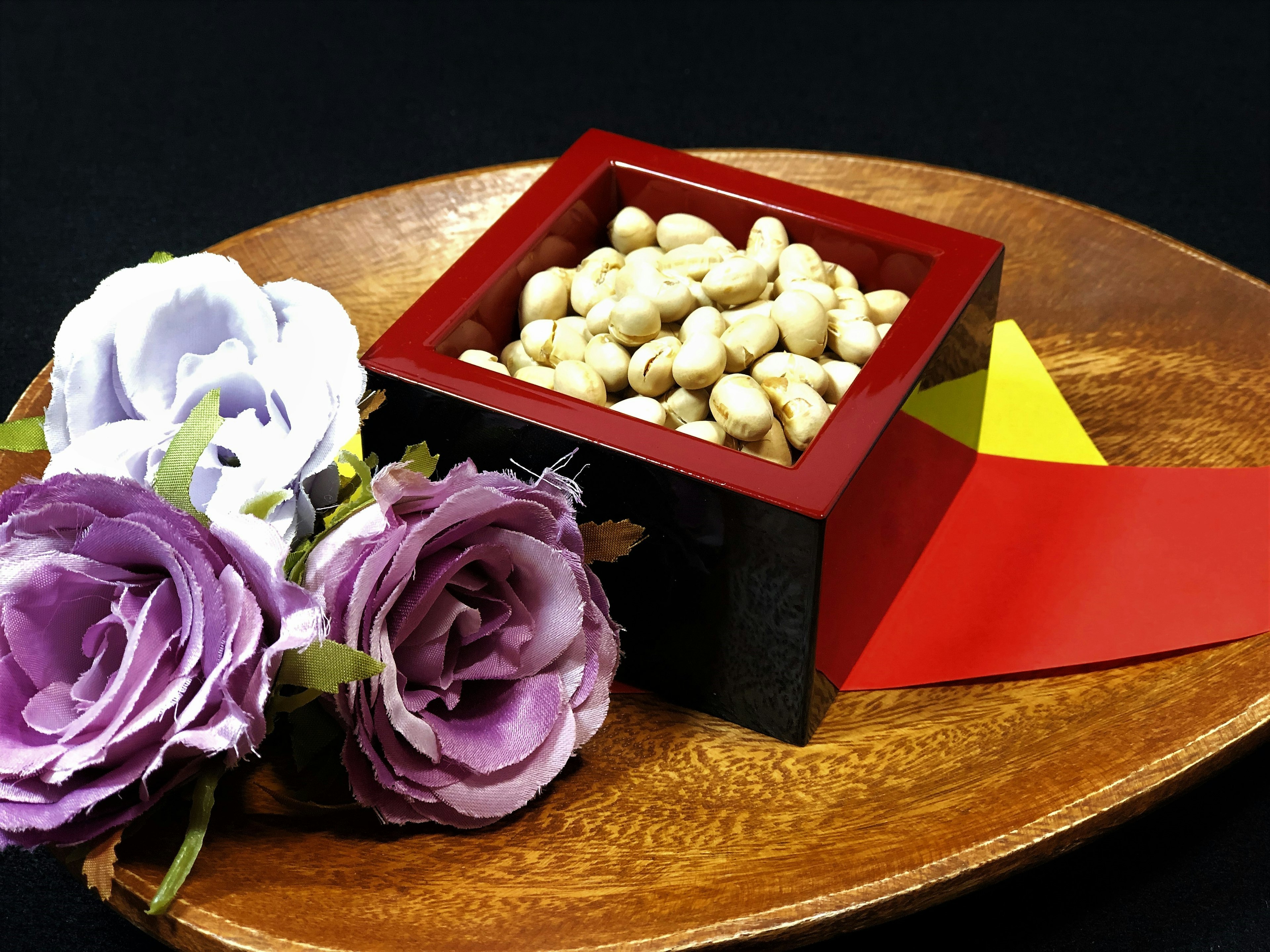 Un plato de madera con una caja roja llena de frijoles blancos y flores moradas