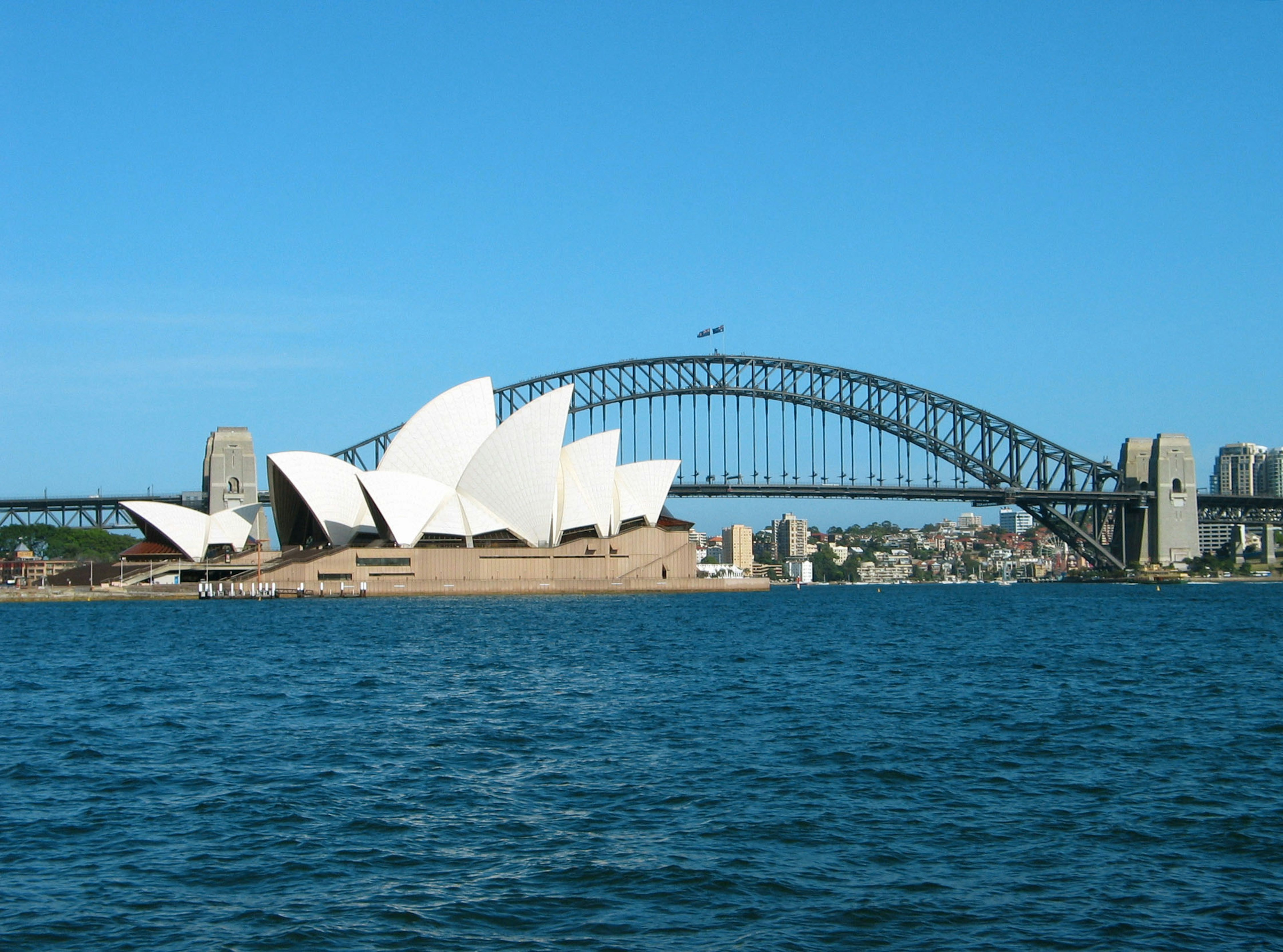 Sydney Opera House mit der Harbour Bridge im Hintergrund und blauem Wasser