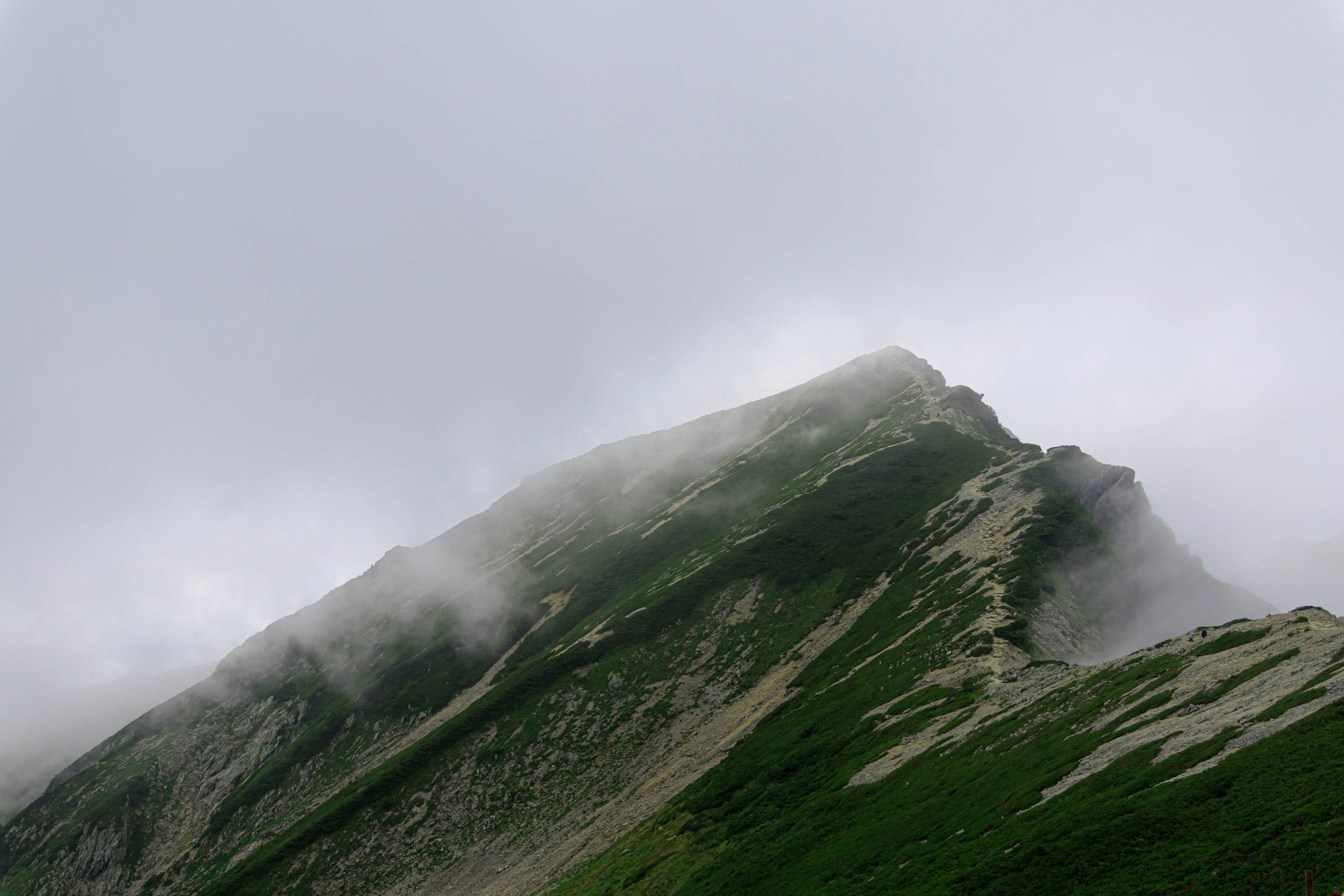 Mountain peak shrouded in mist with green slopes and cloudy sky