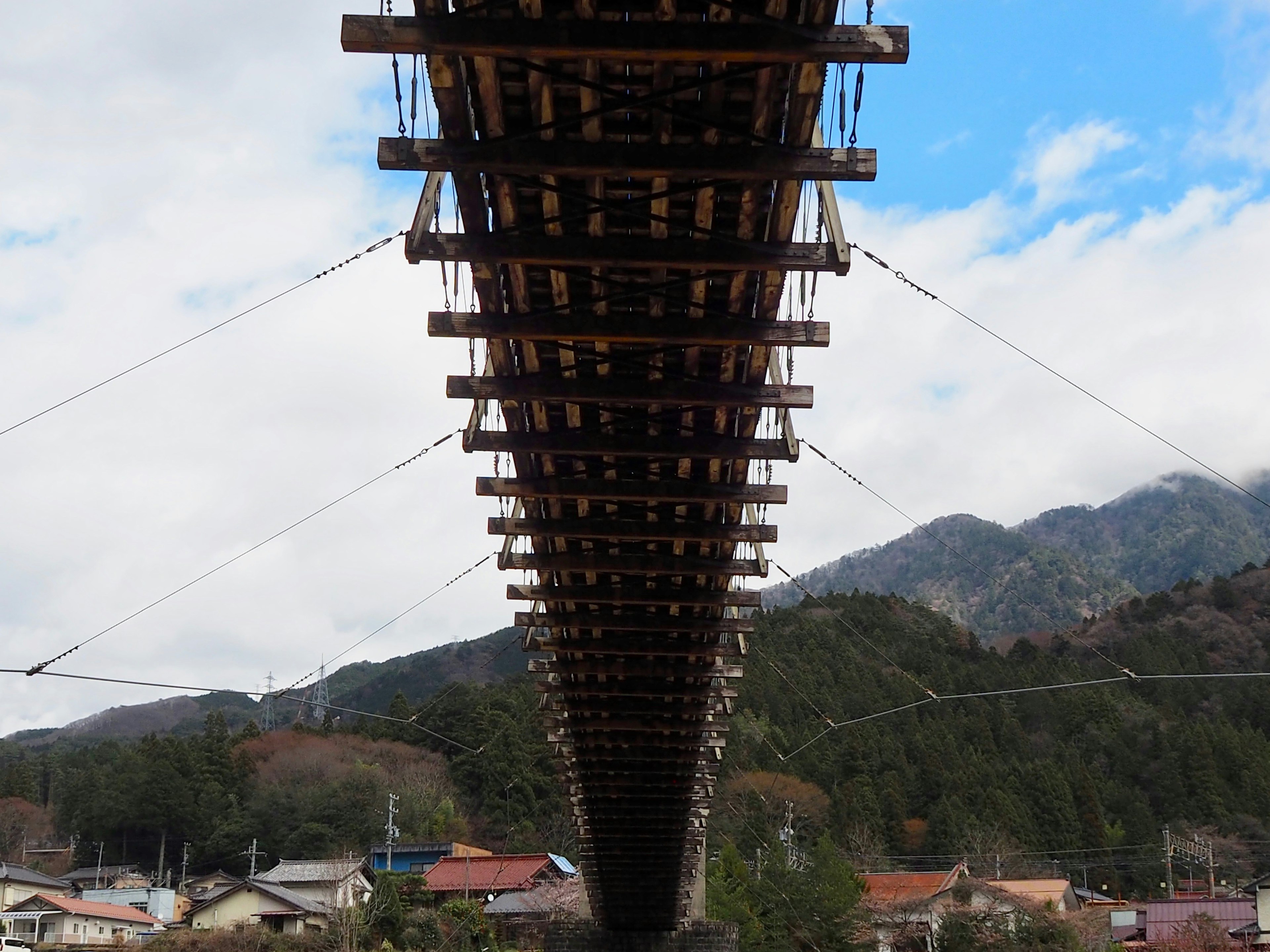 Vue d'un pont par en dessous montrant sa structure avec des montagnes et un ciel bleu en arrière-plan