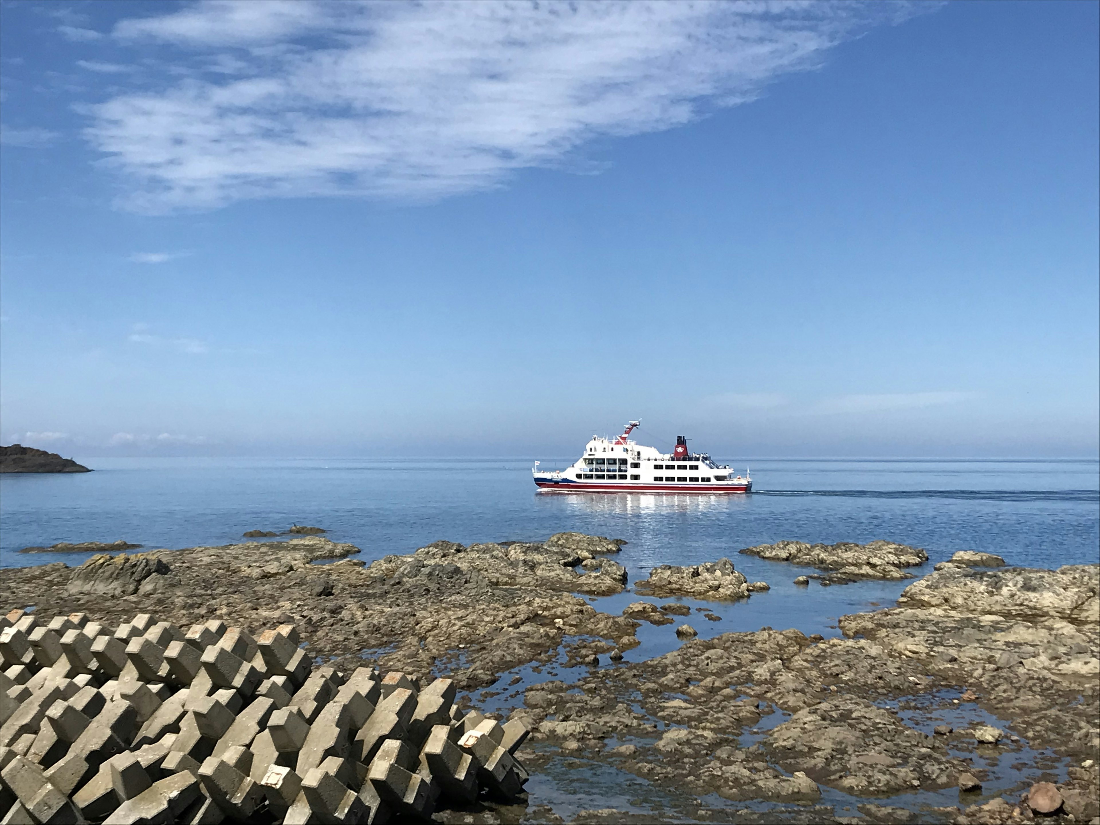 Sebuah perahu putih mengapung di perairan tenang dengan garis pantai berbatu