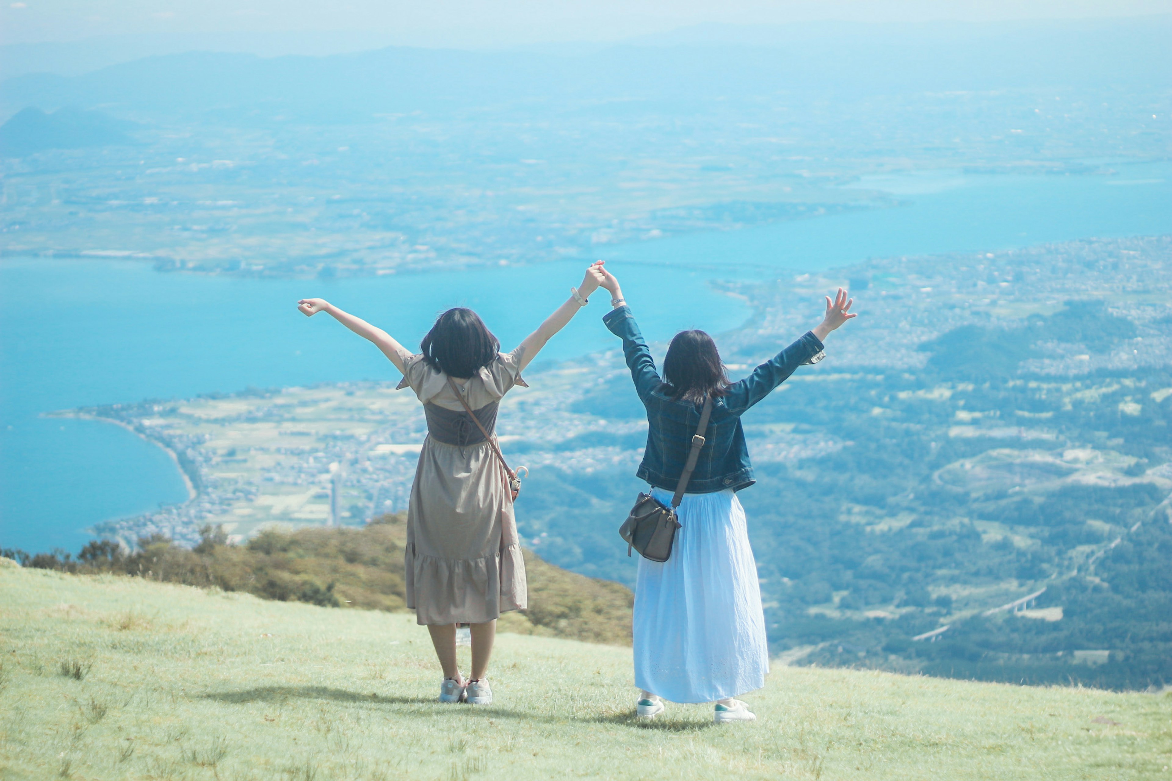 Deux femmes debout au sommet d'une montagne avec les mains levées devant un paysage pittoresque