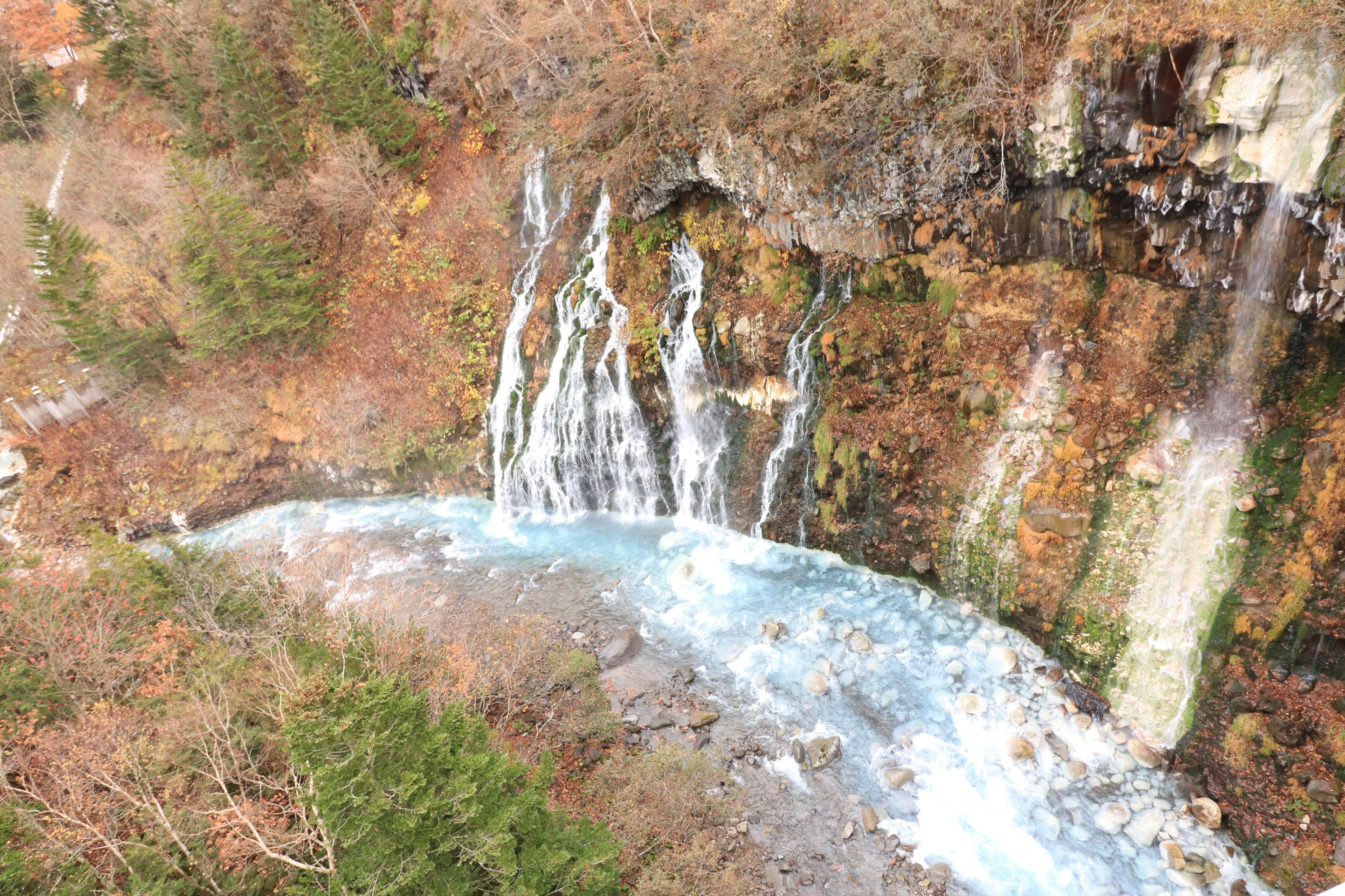 Vista escénica de una cascada que cae en un río rodeado de follaje otoñal