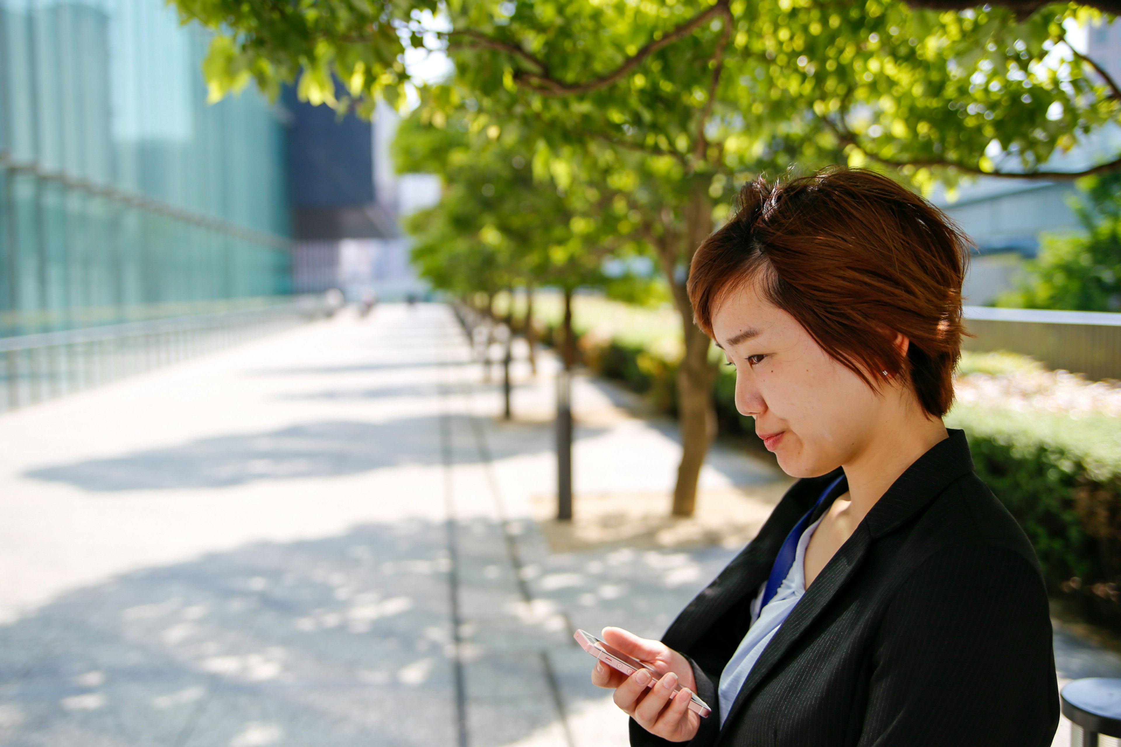 緑の木々の下でスマートフォンを使う女性ビジネスパーソン