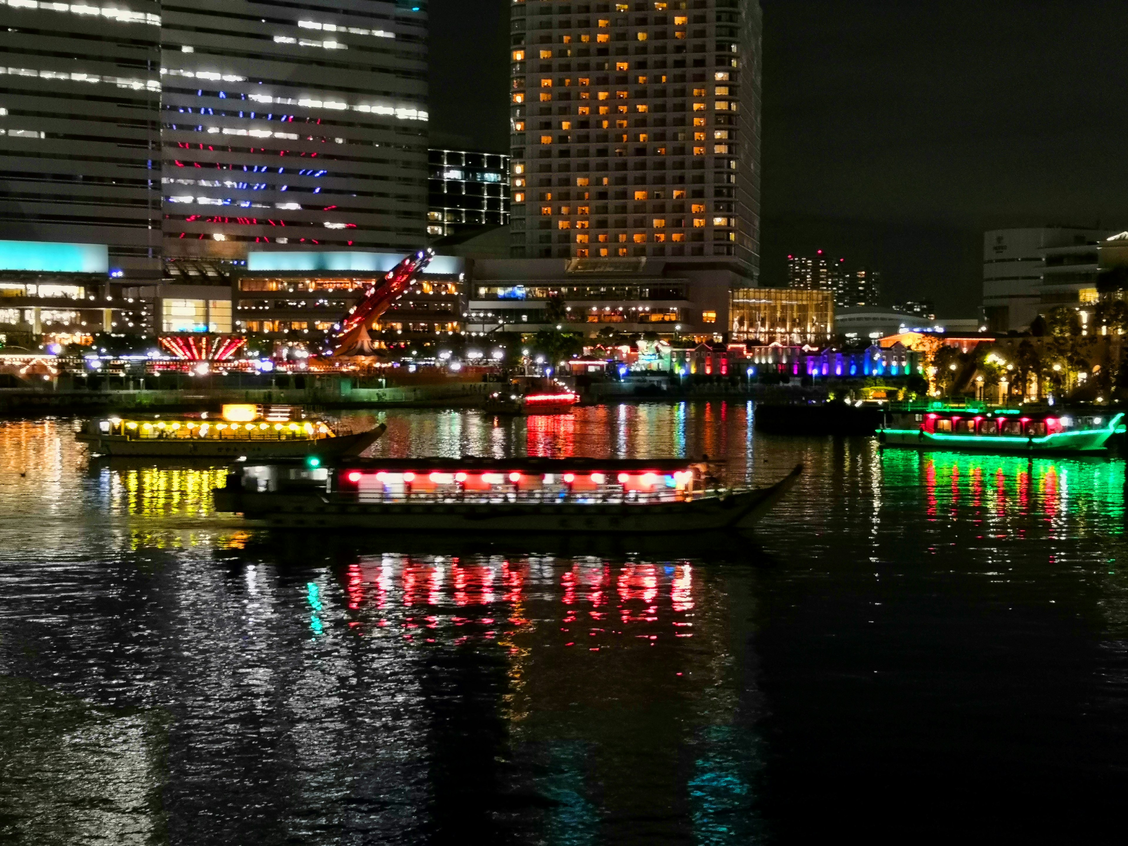 Barcos coloridos en el río por la noche con un brillante horizonte urbano