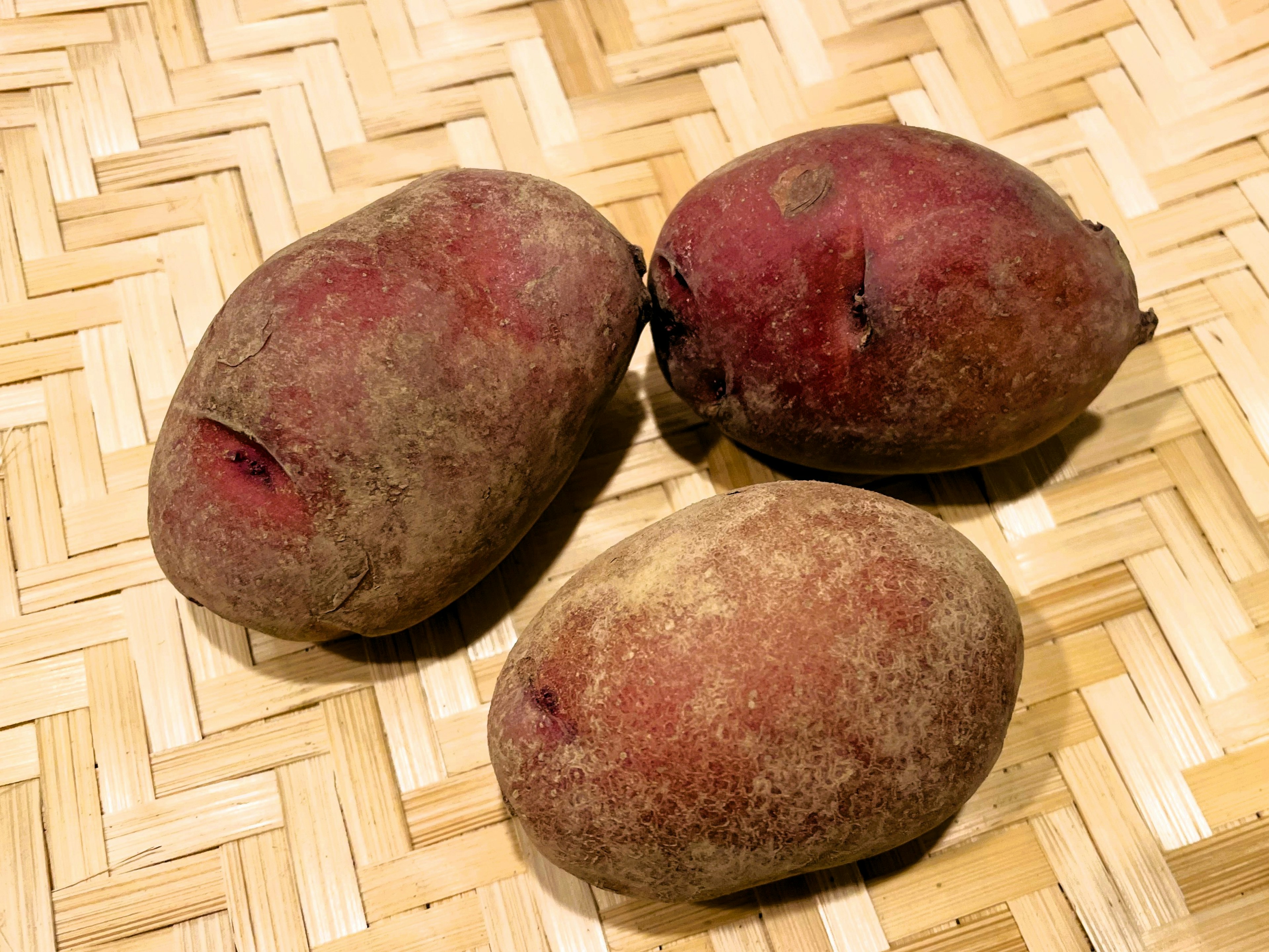 Three reddish sweet potatoes placed on a woven basket