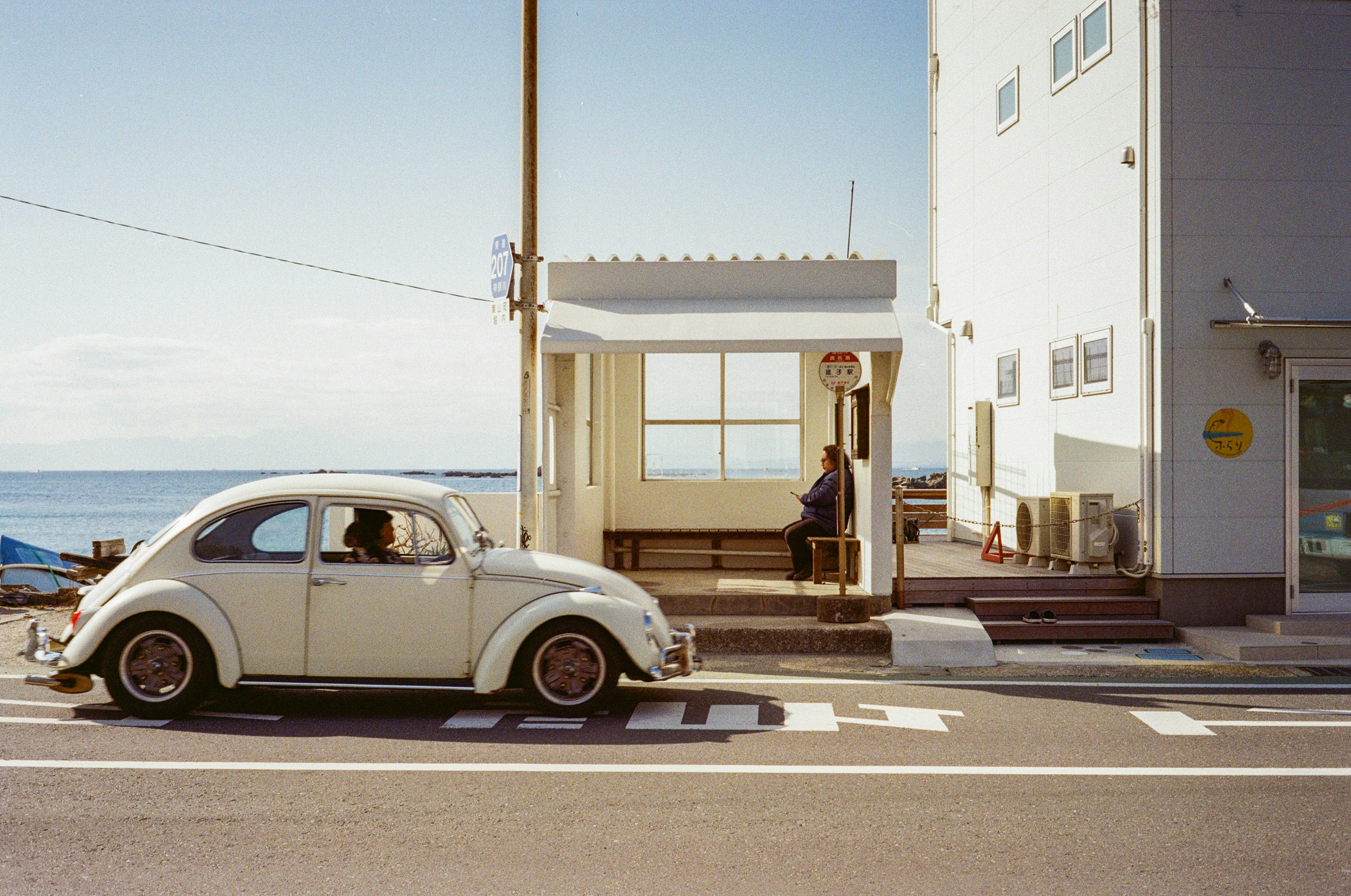 Scenic view of a bus stop by the sea with a vintage white Beetle car