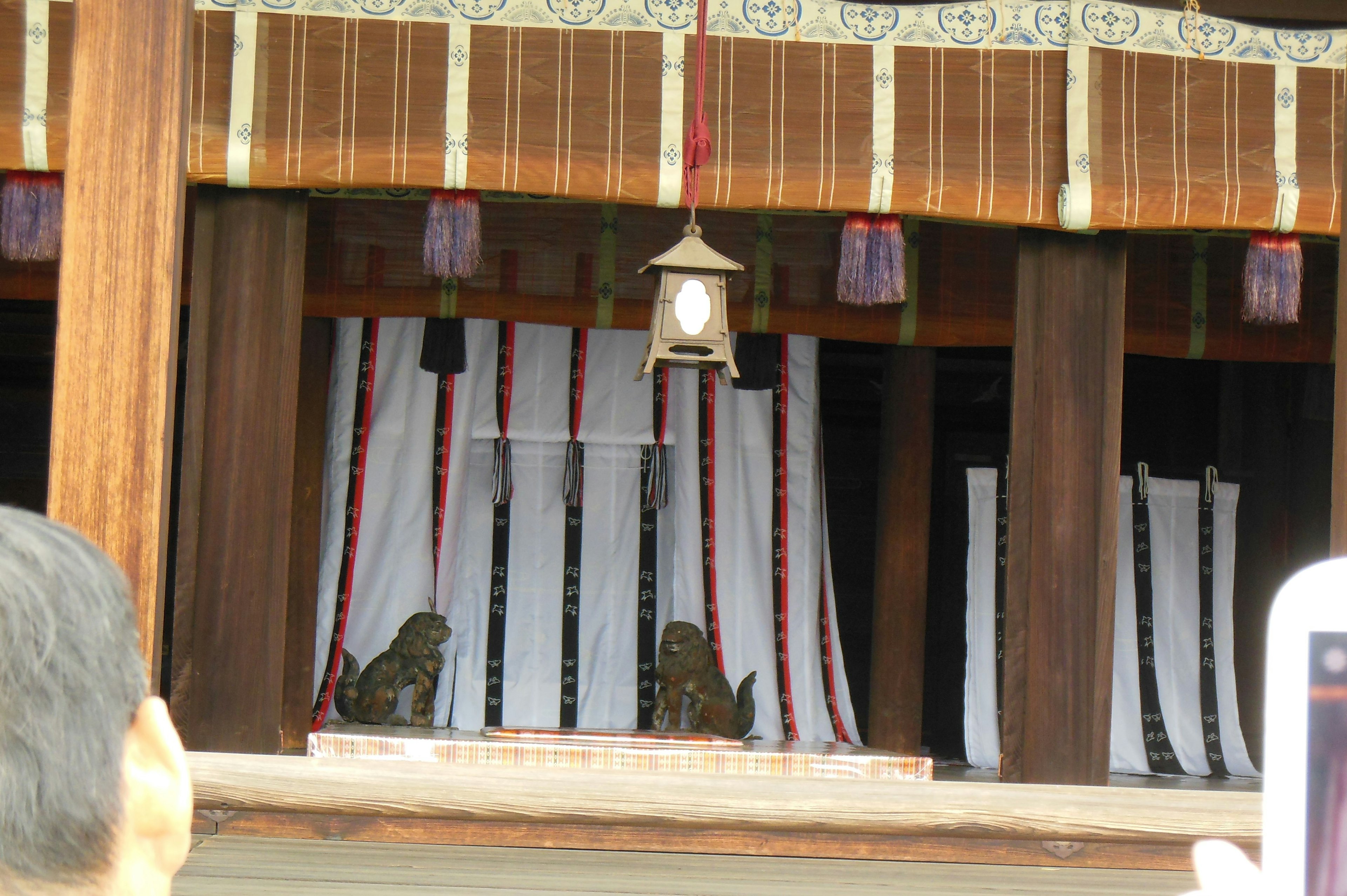 Photo of a shrine interior featuring wooden pillars and white fabric with a hanging lantern