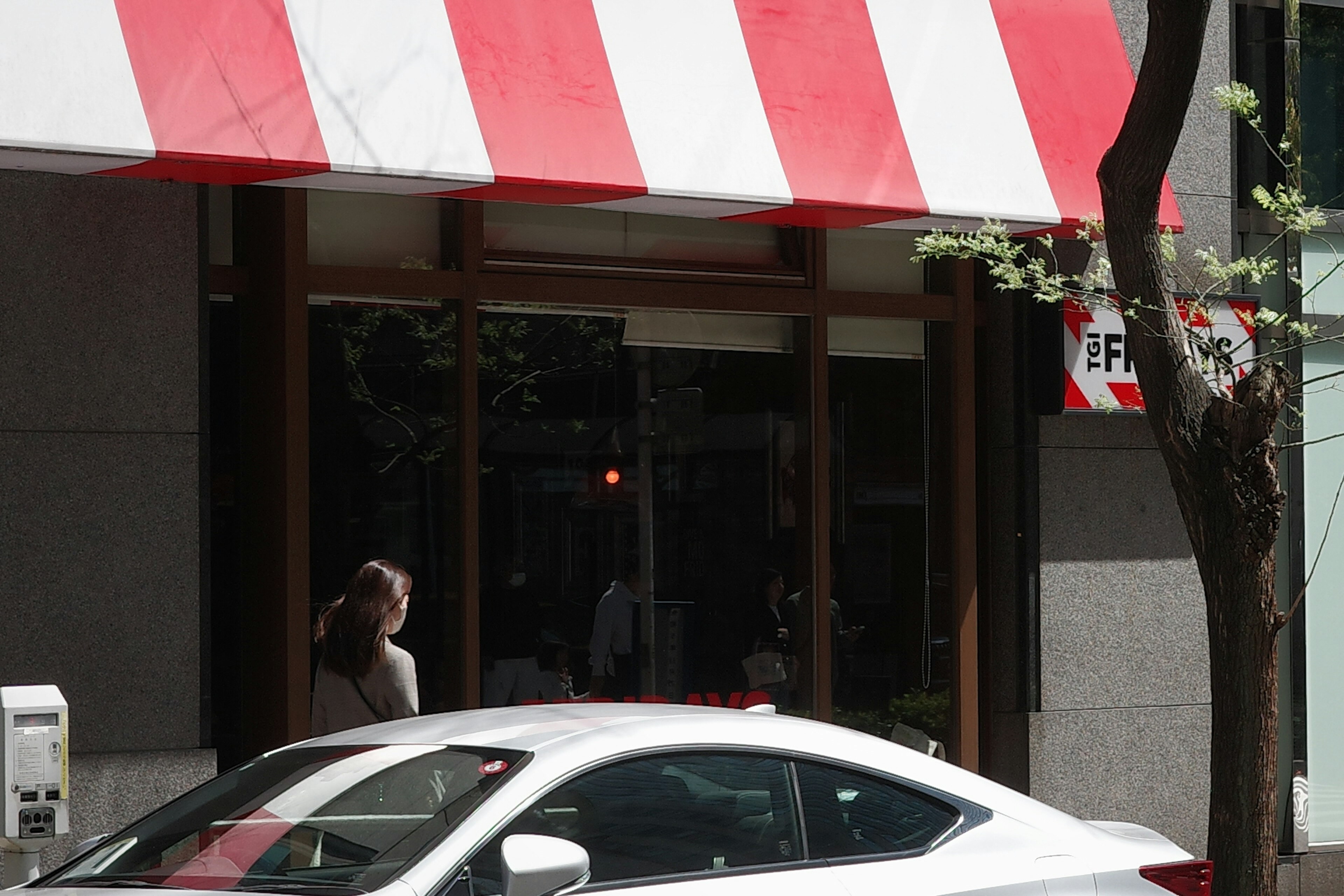 Store entrance beneath red and white striped awning with a white car