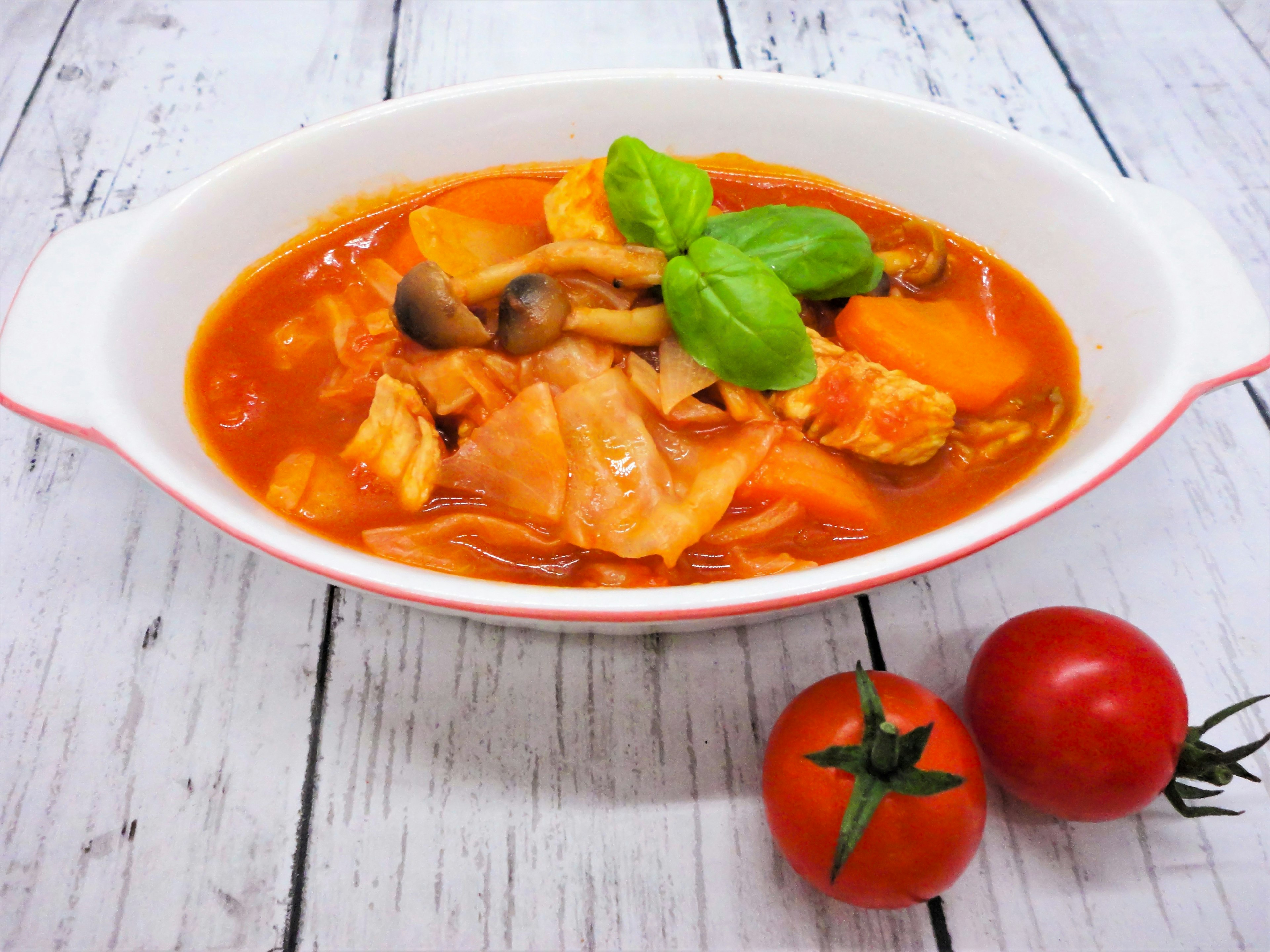 Soupe à base de tomates servie dans un plat blanc garnie de basilic frais et de légumes