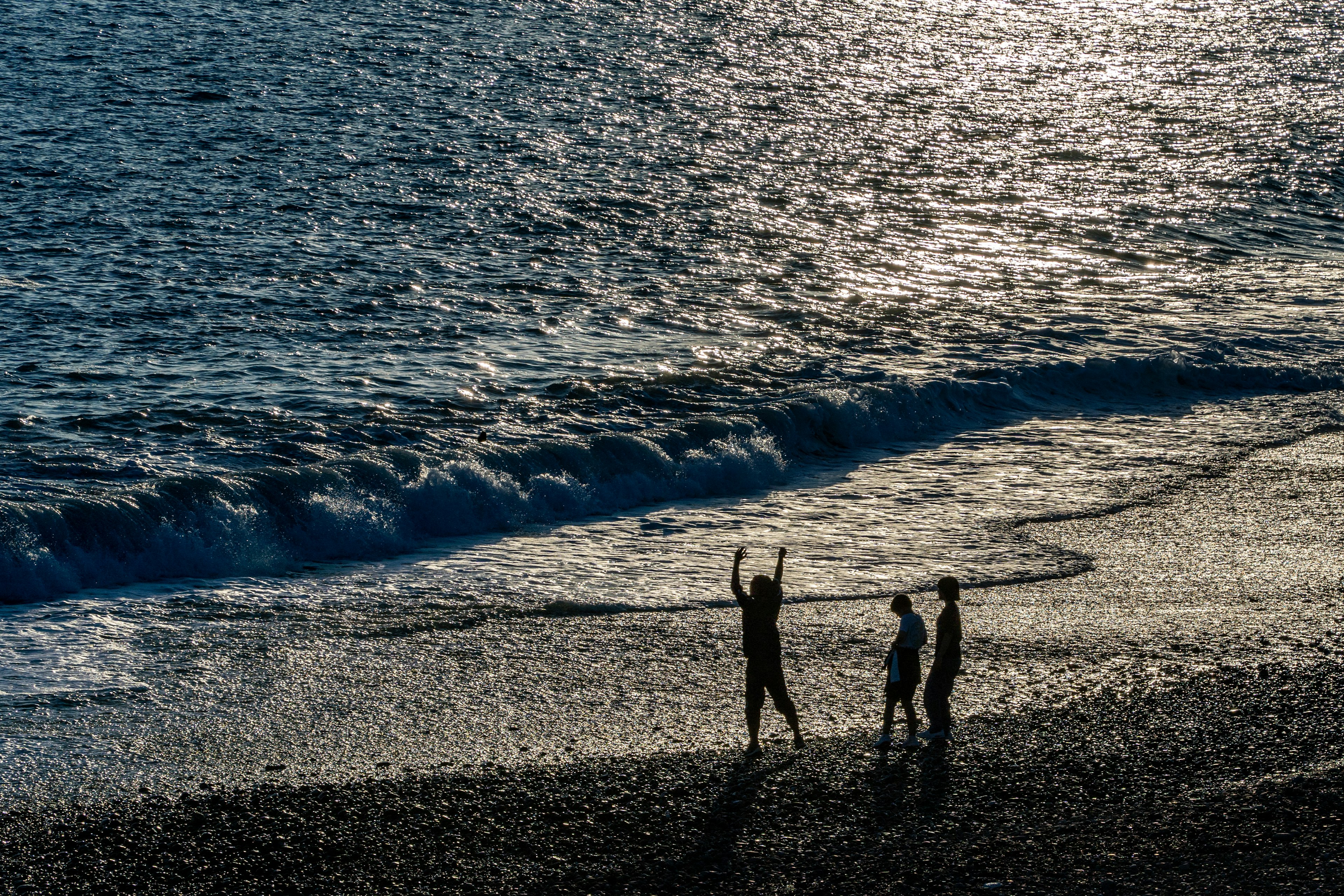 Siluet anak-anak bermain di pantai dengan ombak berkilau