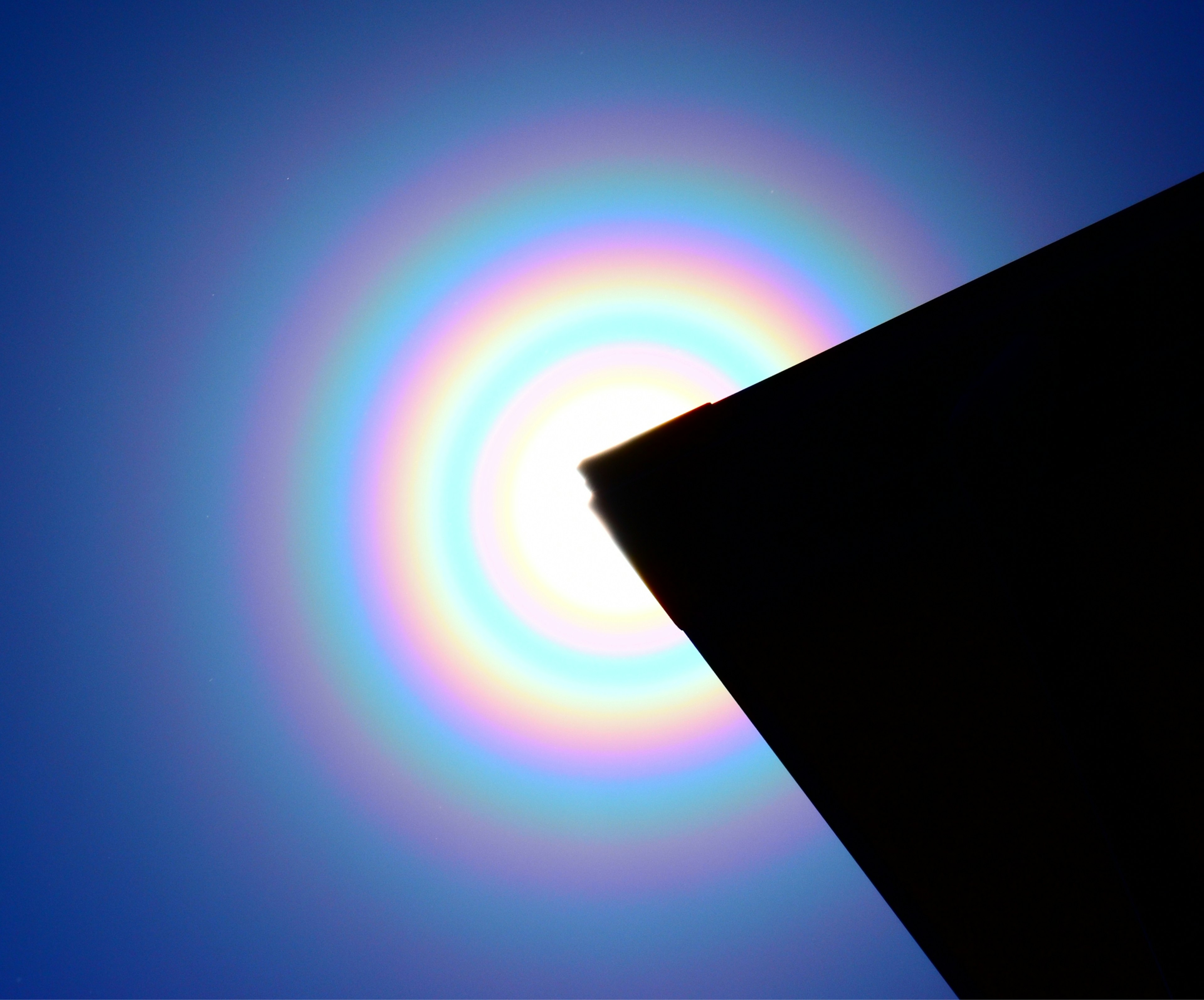 Rainbow halo around the sun with a silhouette of a building edge