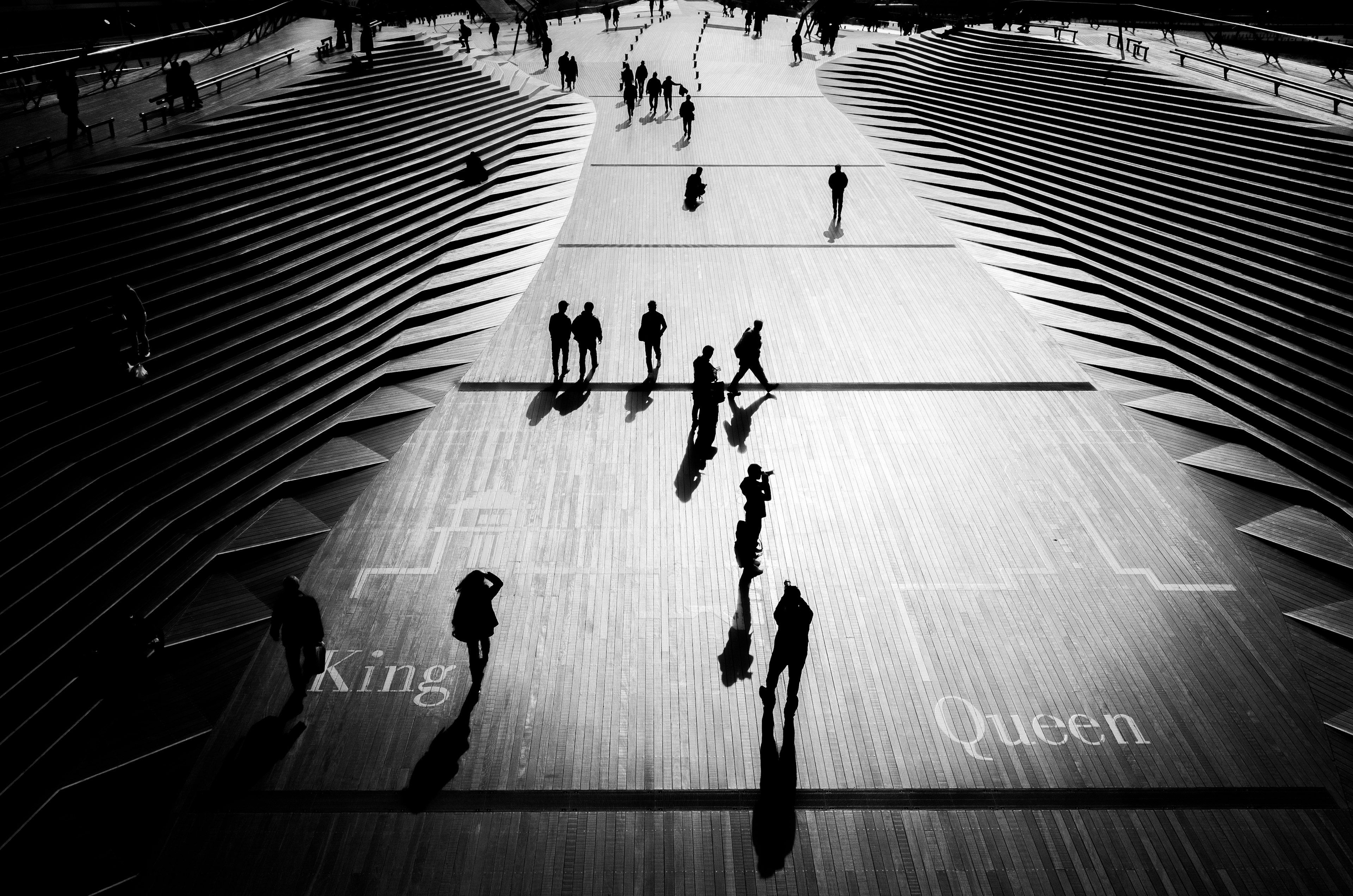 Aerial view of people walking on stairs with striking shadows in black and white featuring the words King and Queen