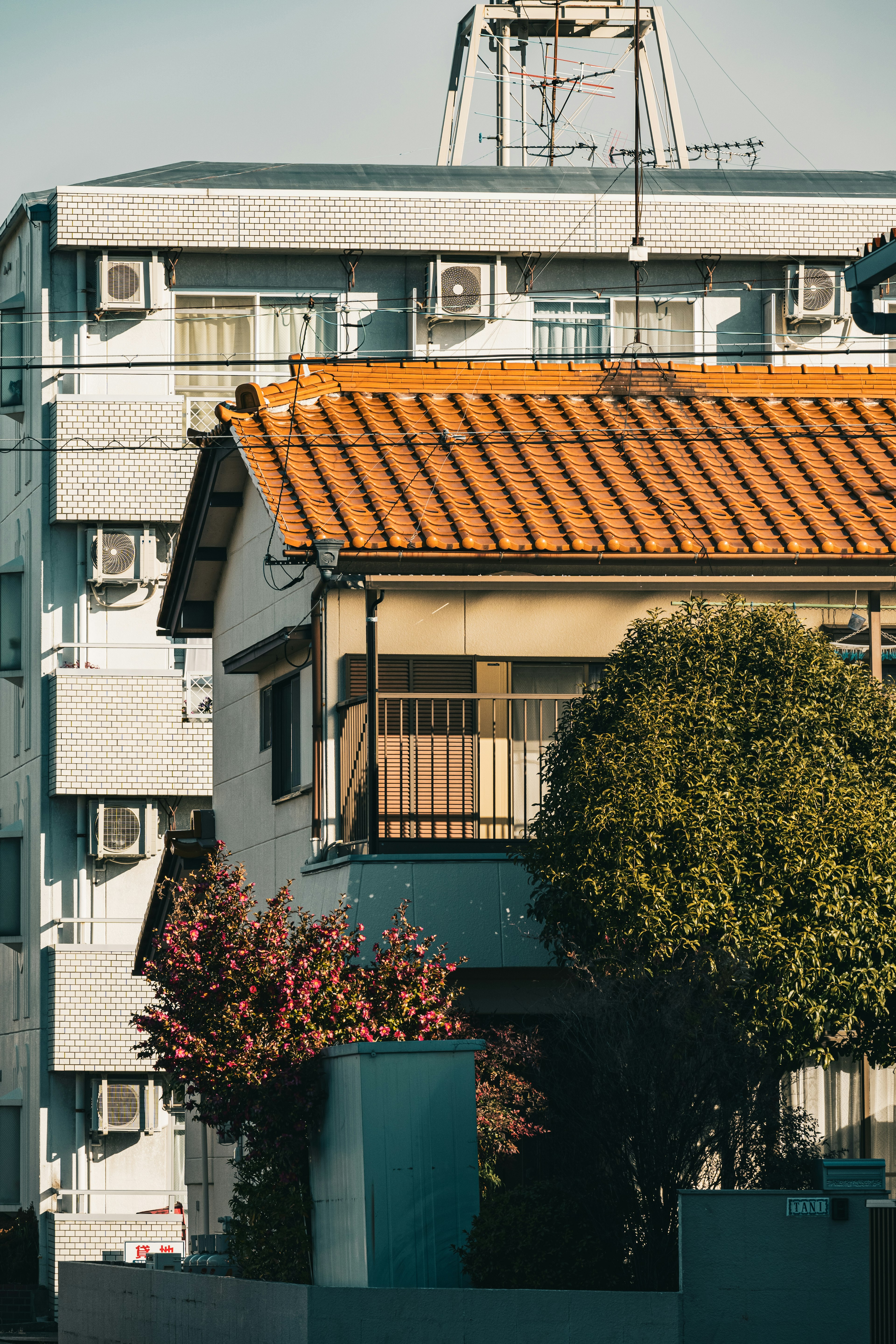 A house with an orange roof next to a building featuring air conditioning units and flowering trees