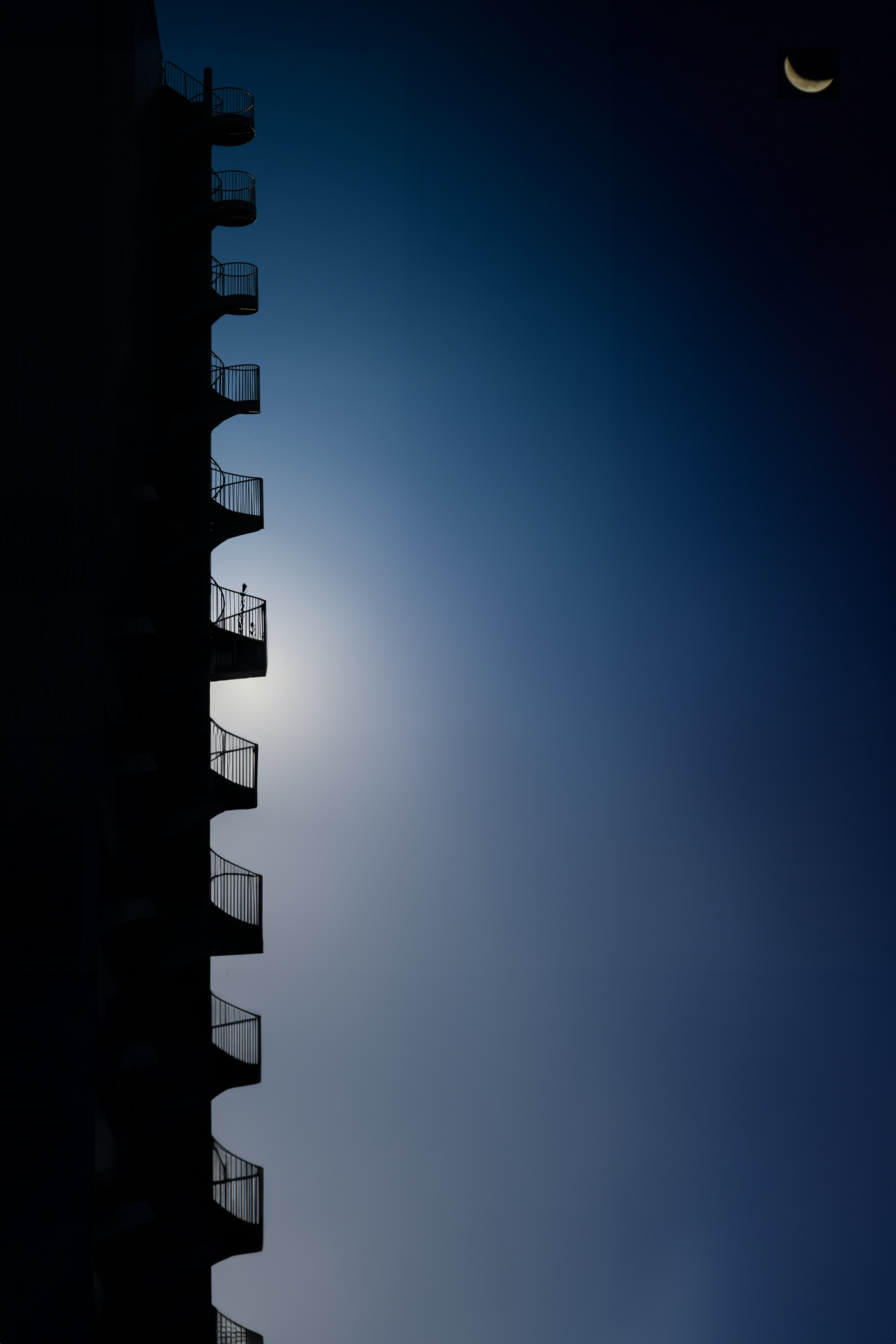 Balcones en silueta contra un cielo nocturno azul con una luna creciente