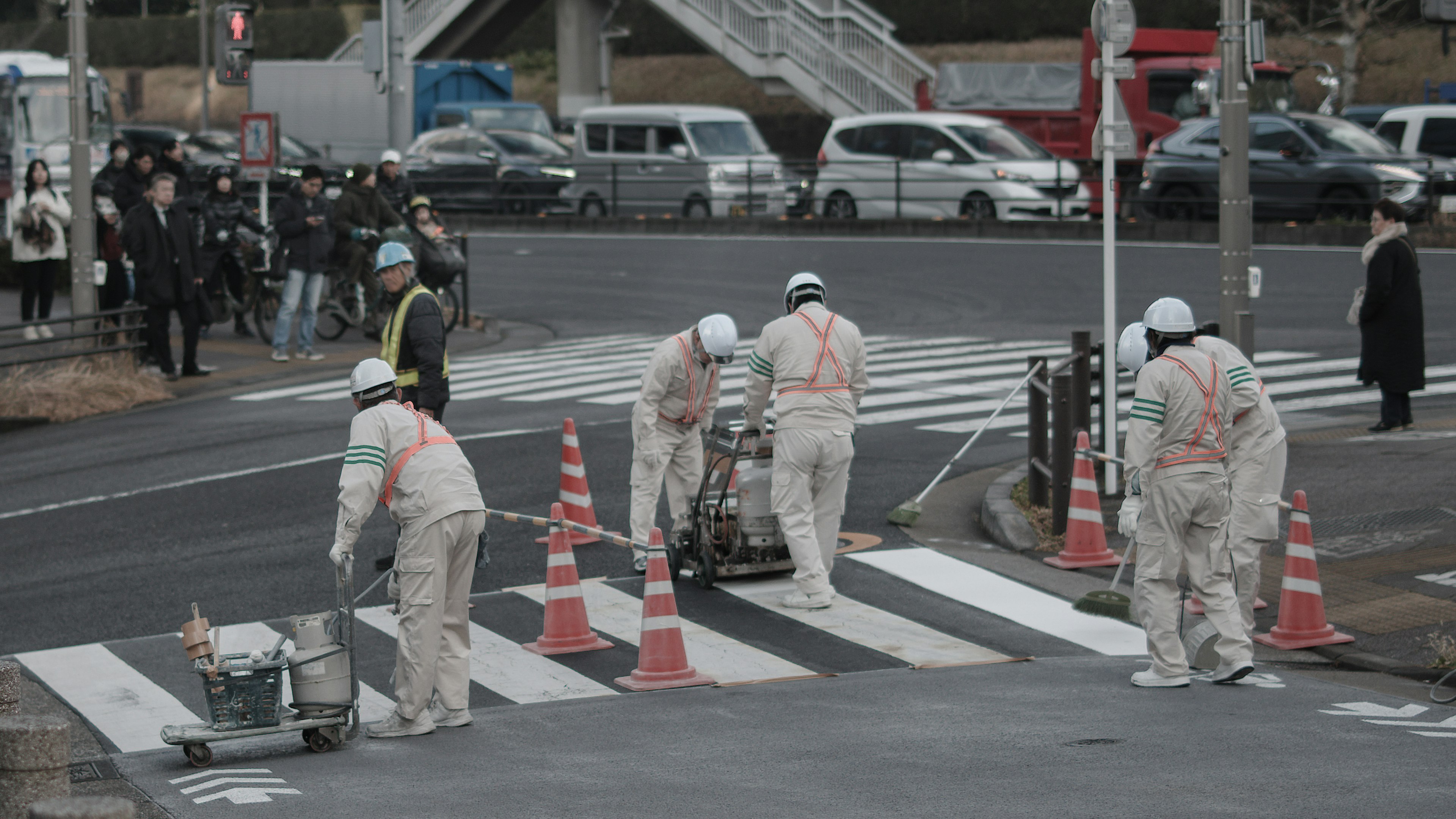 Workers repairing a crosswalk with traffic cones and vehicles in the background