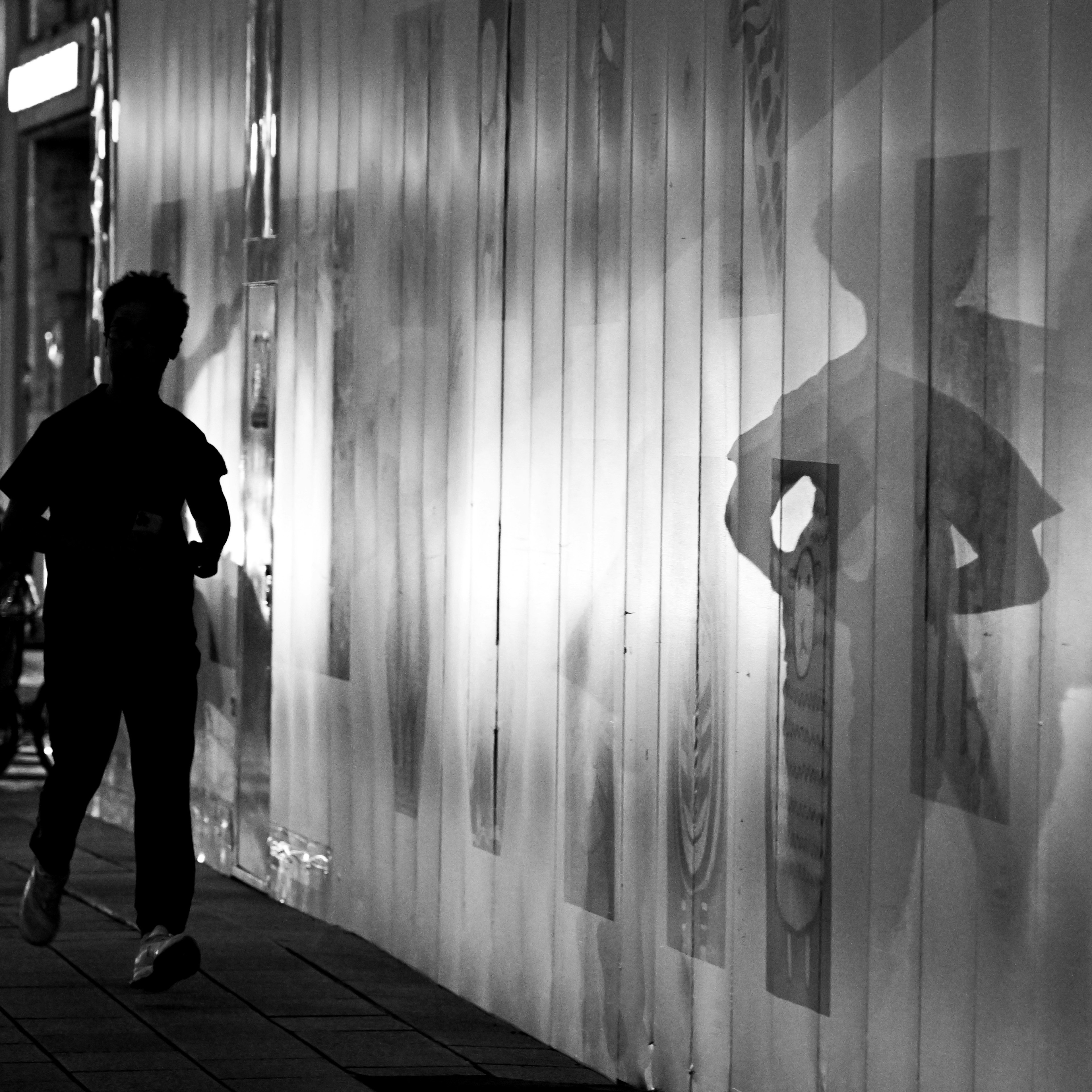 Silhouette seorang anak berlari di sepanjang dinding dengan bayangan kontras dalam hitam dan putih