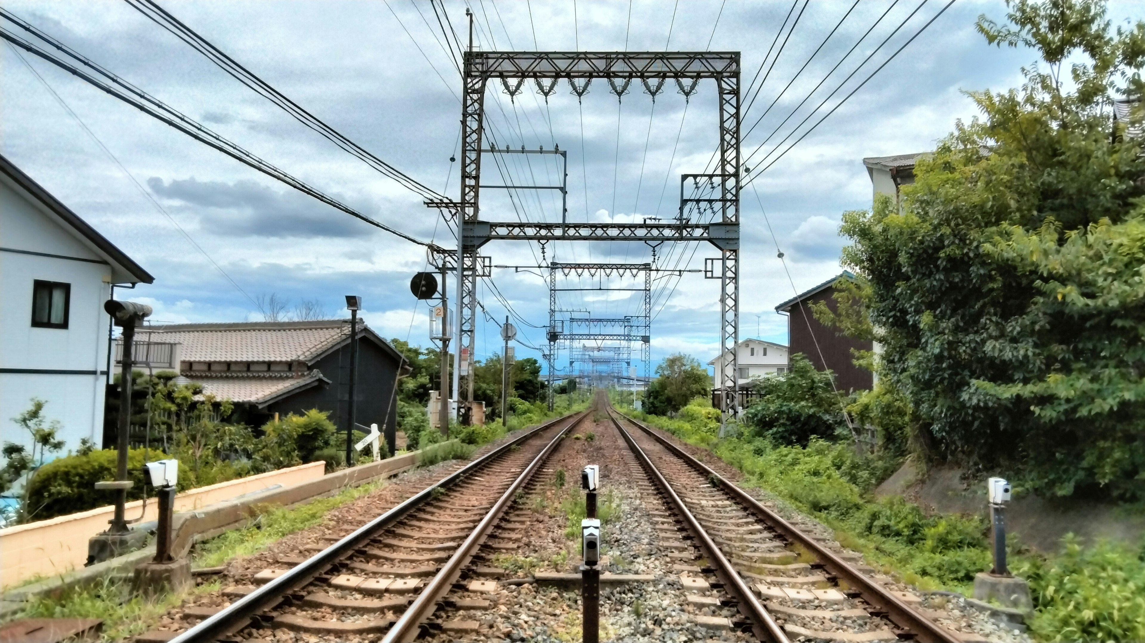 A view of railway tracks with overhead lines and surrounding greenery