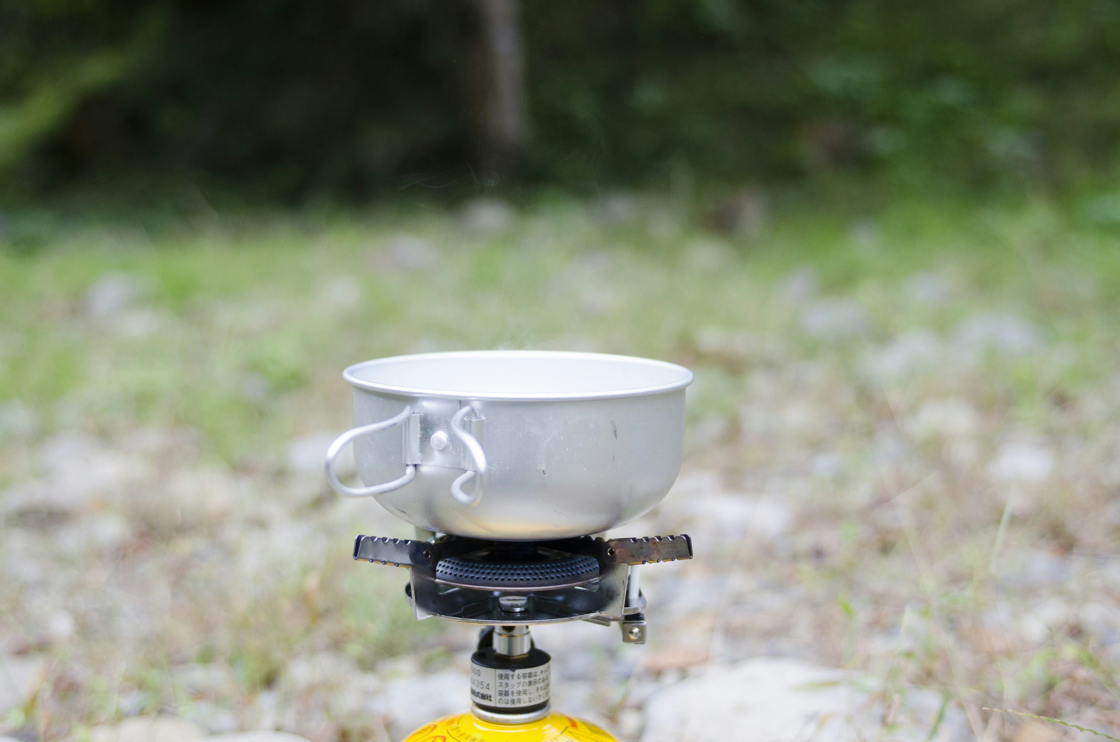 Une casserole blanche posée sur un réchaud en plein air dans une zone herbeuse