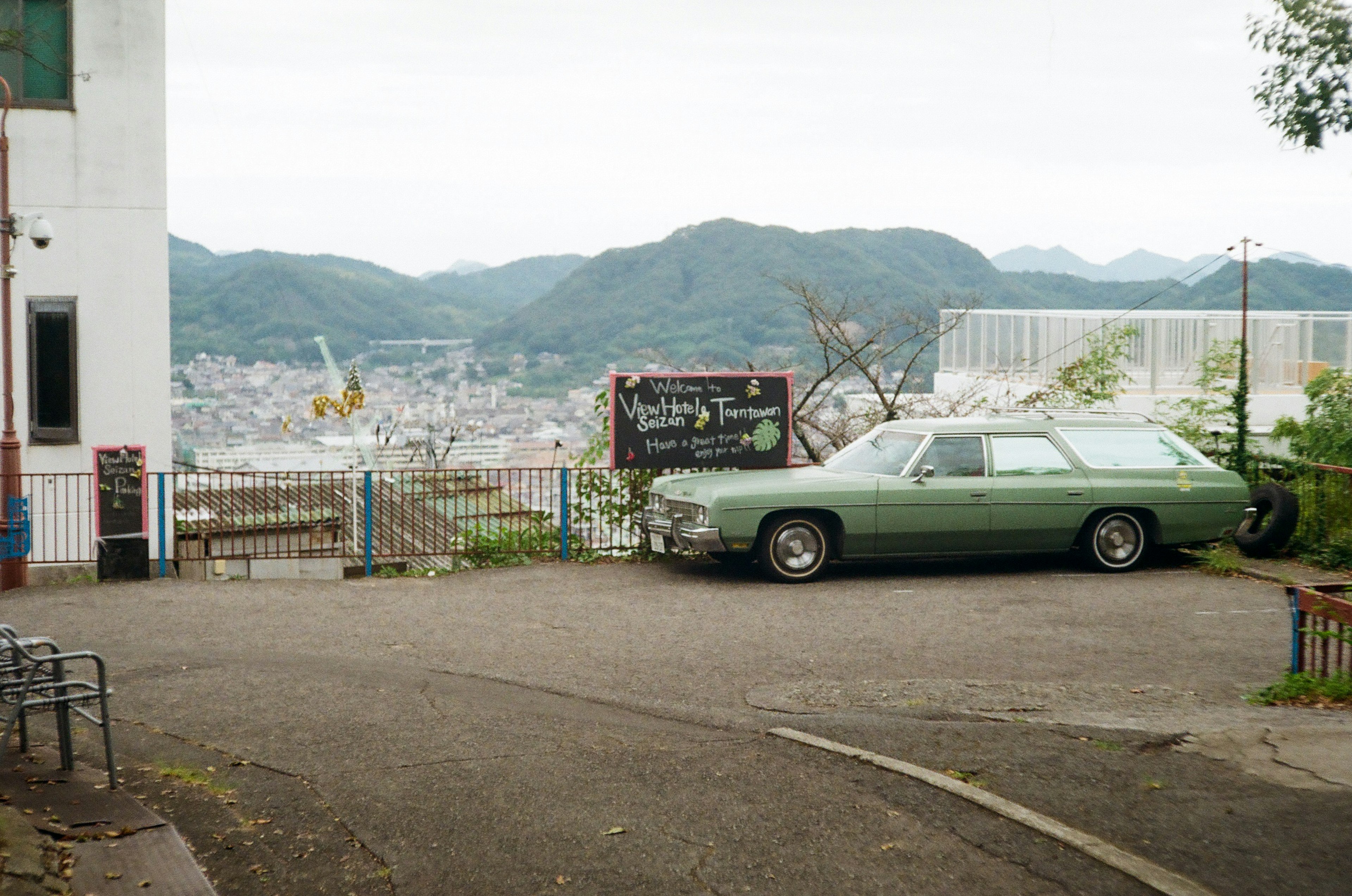 Voiture verte garée avec une vue panoramique sur des montagnes et une ville