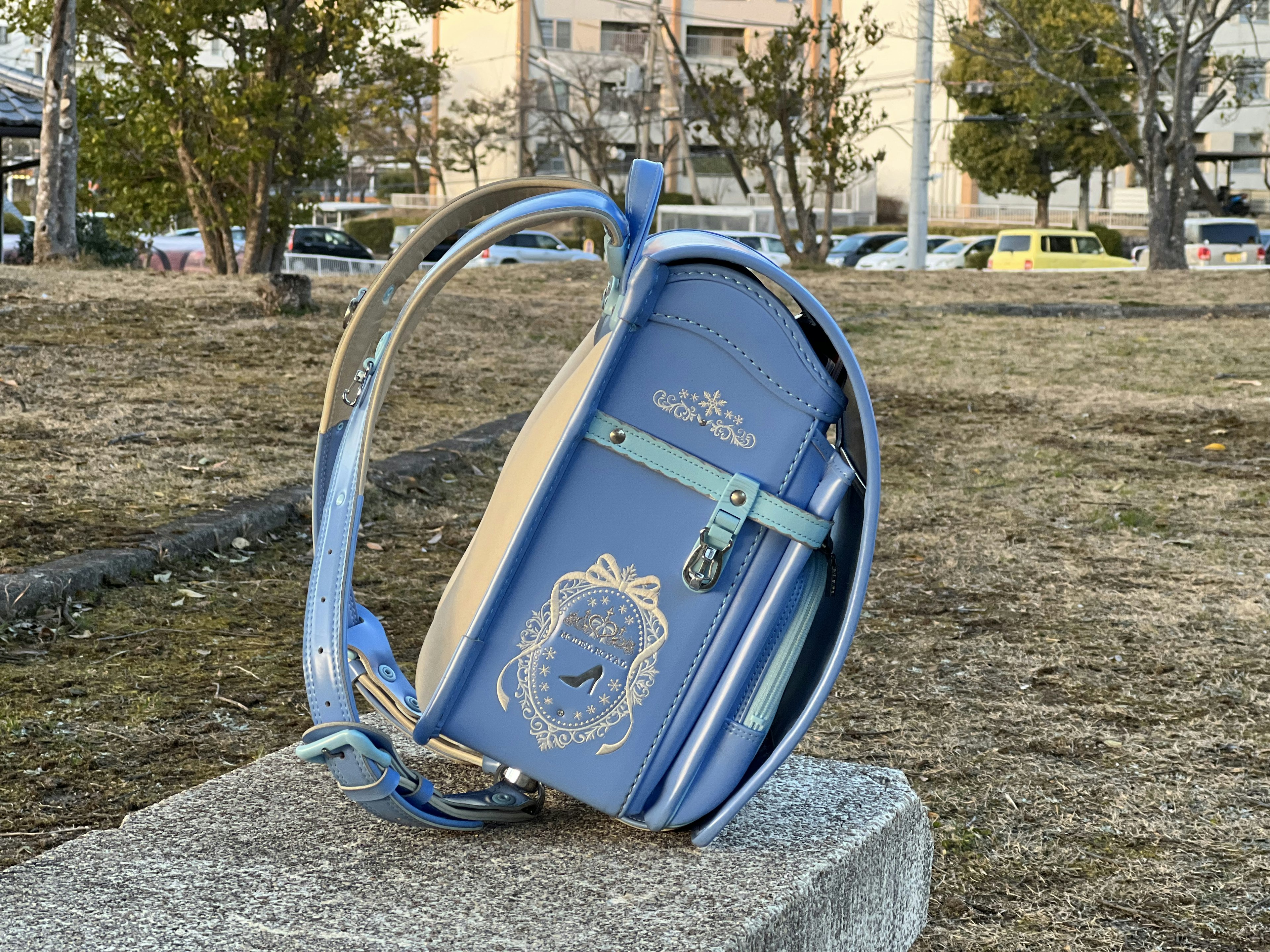 A blue randoseru backpack placed on a stone in a park setting