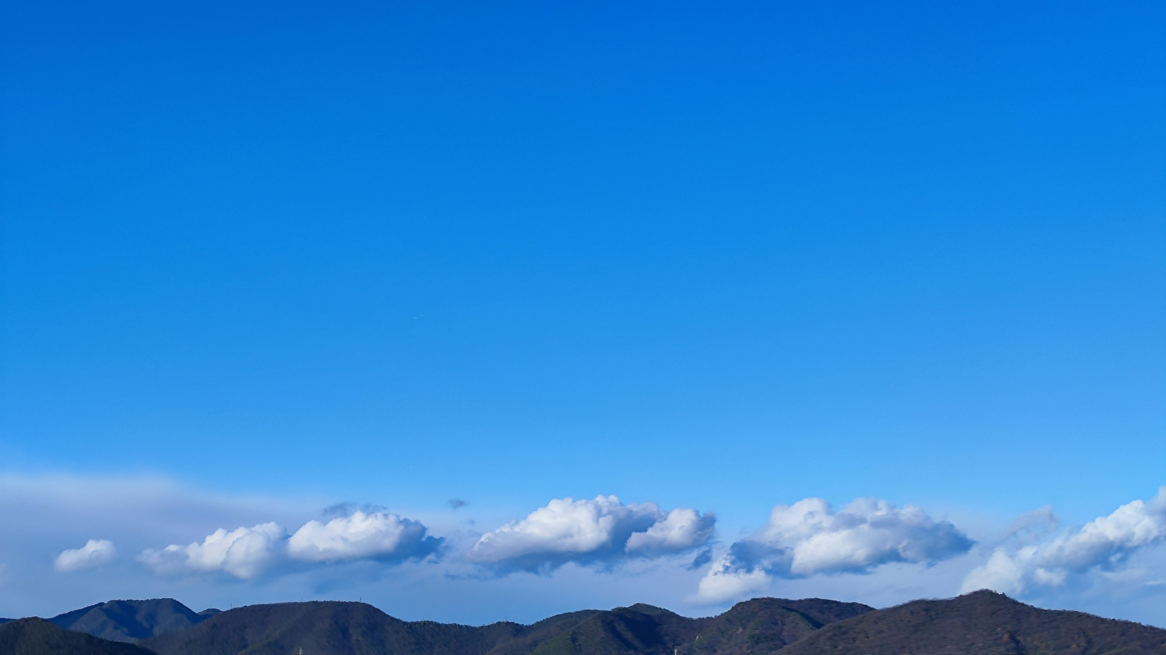 Pemandangan pegunungan di bawah langit biru cerah dengan awan putih