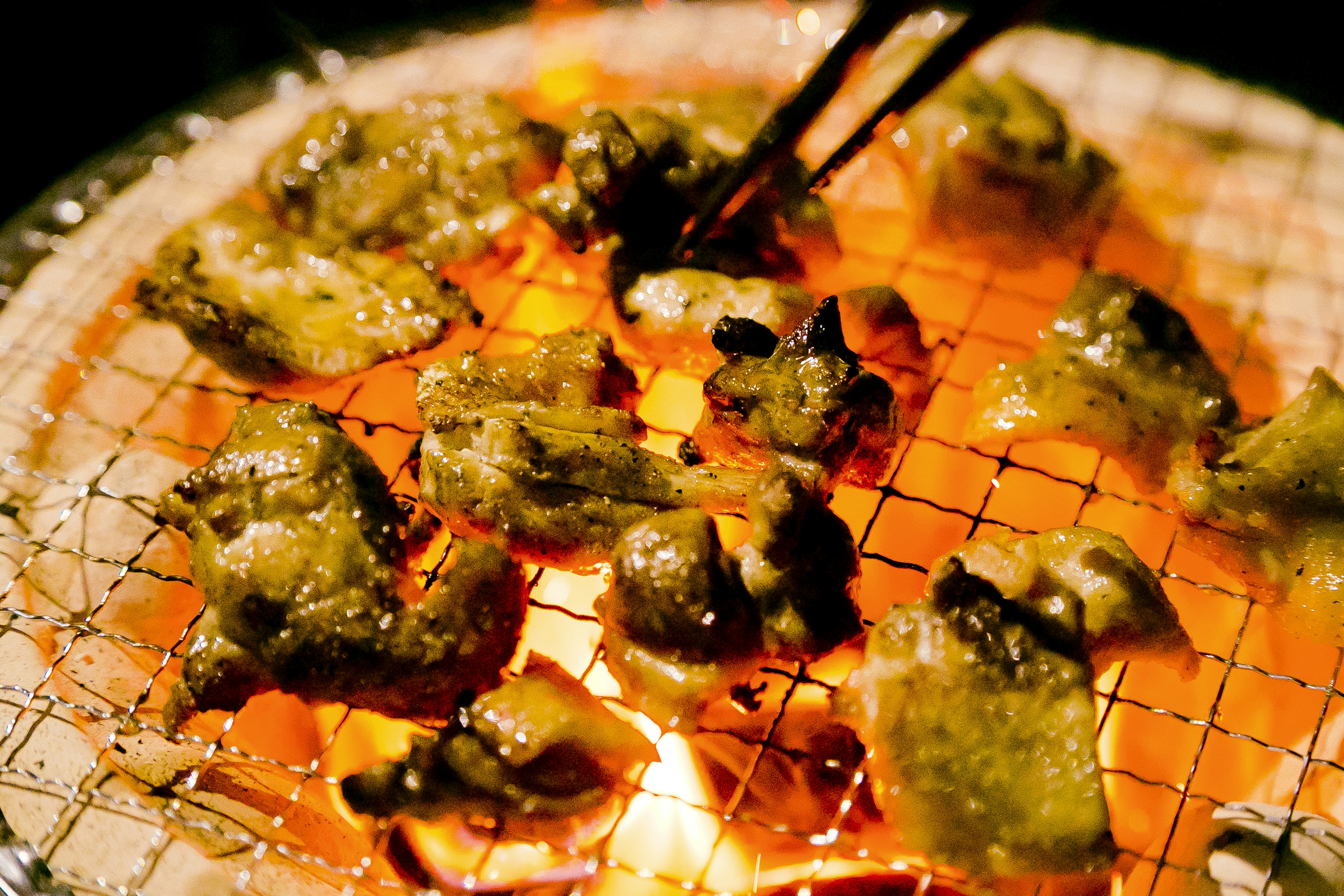 Grilled meat pieces on a charcoal grill with chopsticks