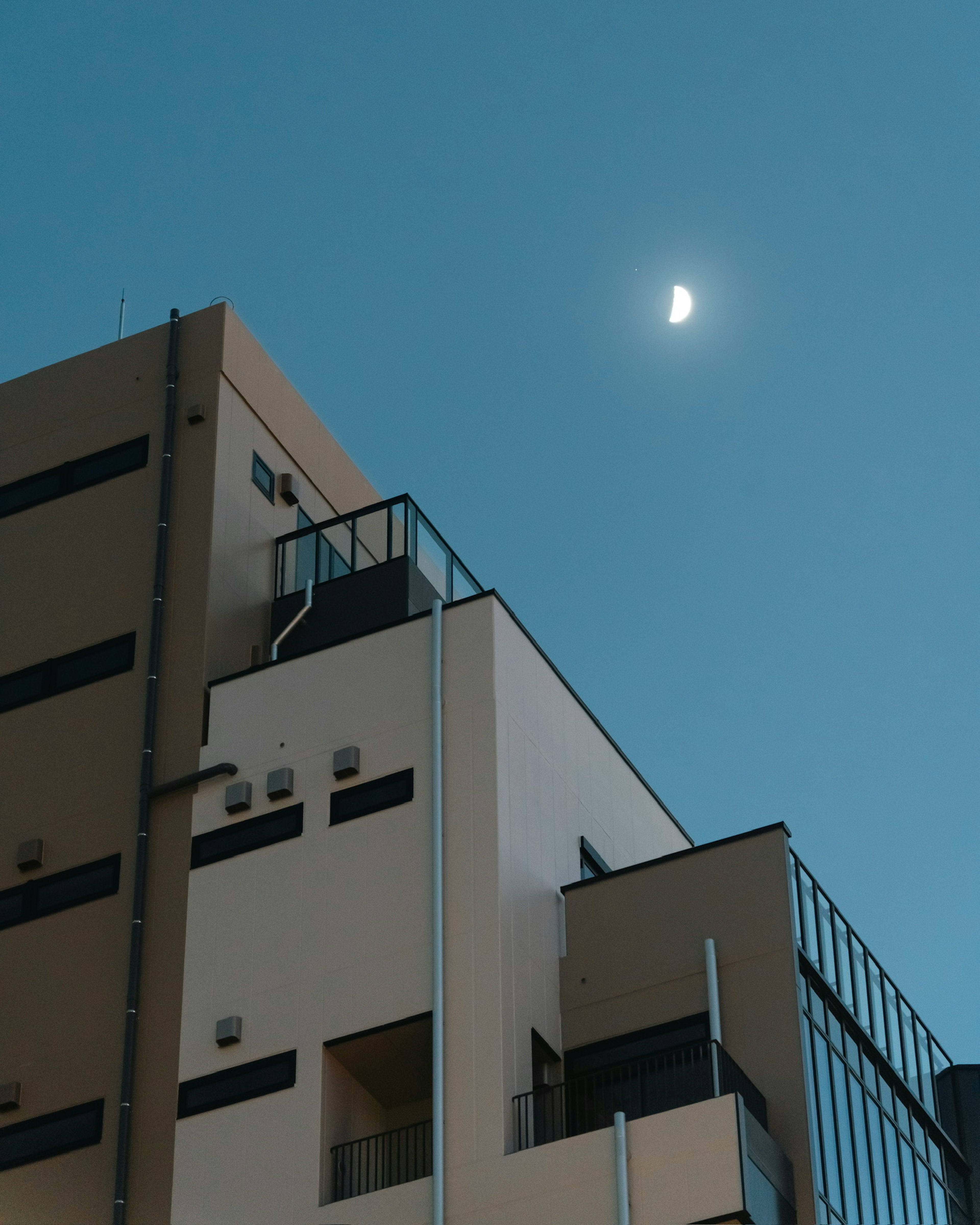 Modernes Gebäude mit Balkonen unter einem klaren blauen Himmel mit einer Mondsichel