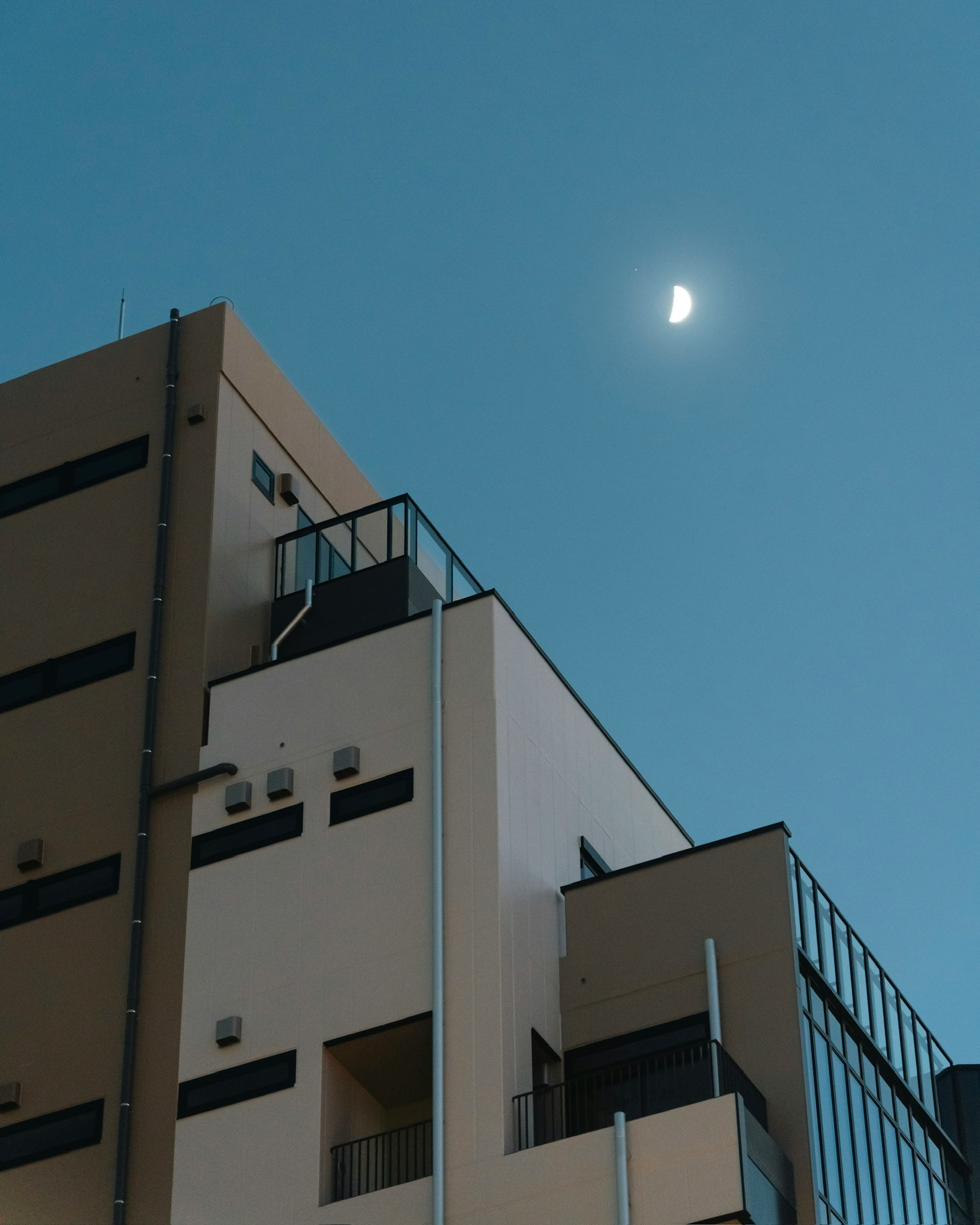 Bâtiment moderne avec balcons sous un ciel bleu clair avec une lune croissante