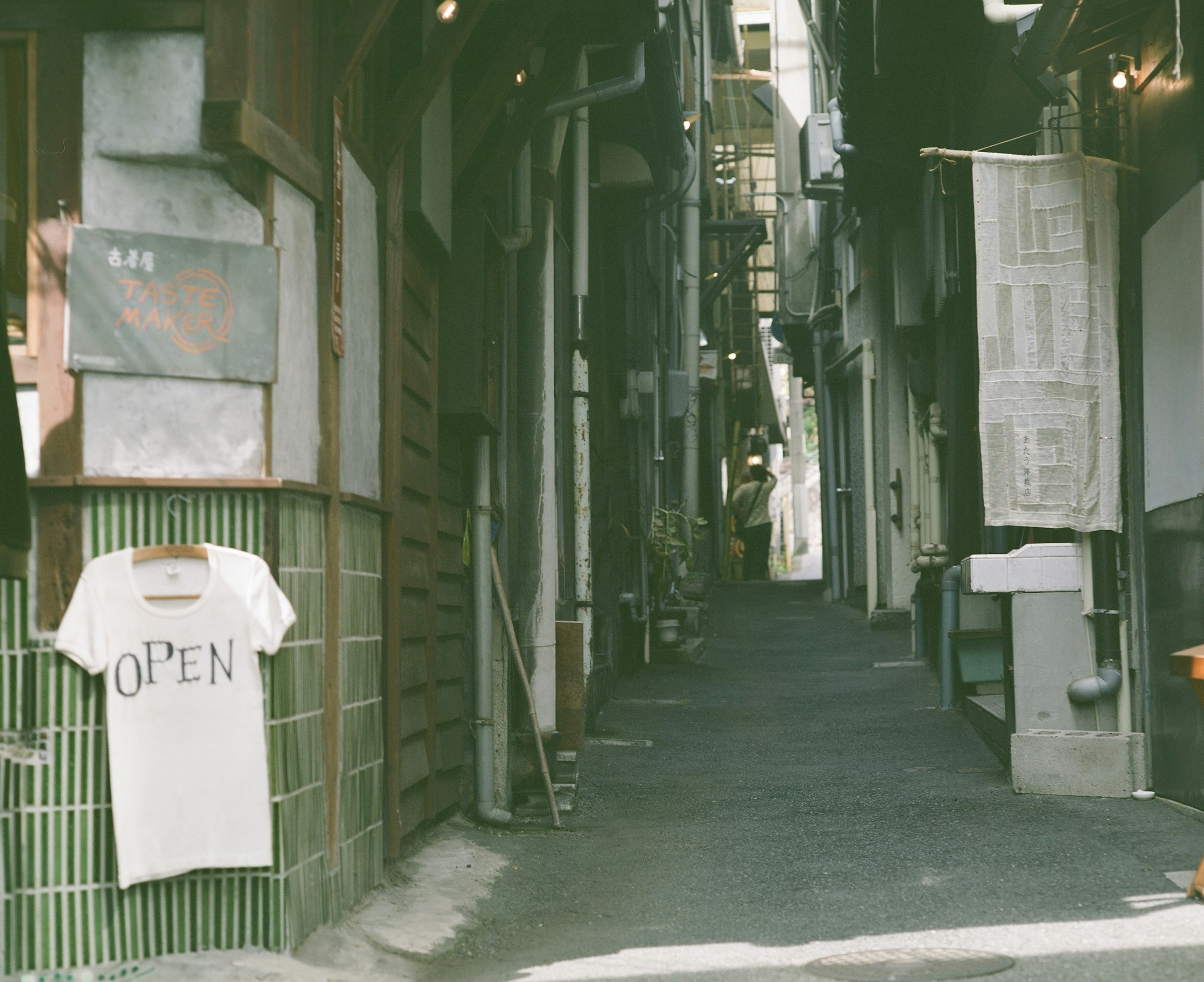 狭い路地にかかる「OPEN」と書かれたTシャツと古い建物が描かれた風景