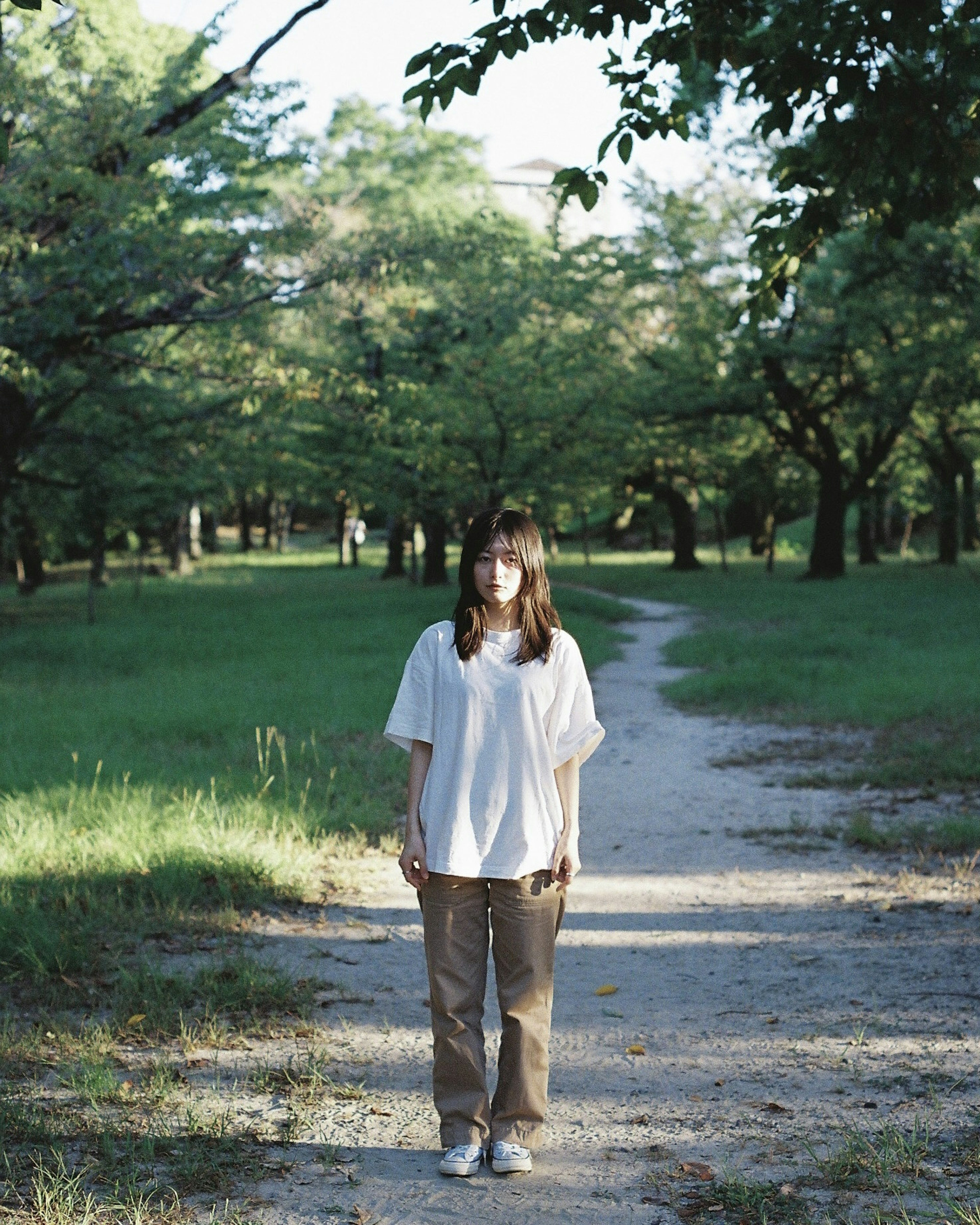 Portrait d'une femme debout sur un chemin de parc entouré d'arbres verts et de lumière douce