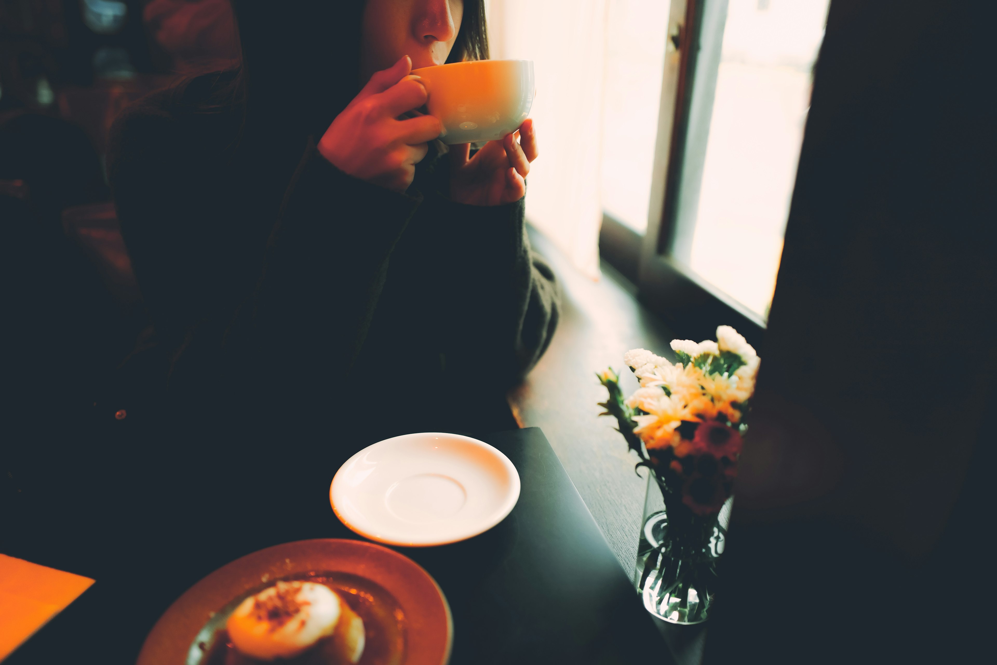 Mujer bebiendo café en una acogedora cafetería con comida y flores en la mesa