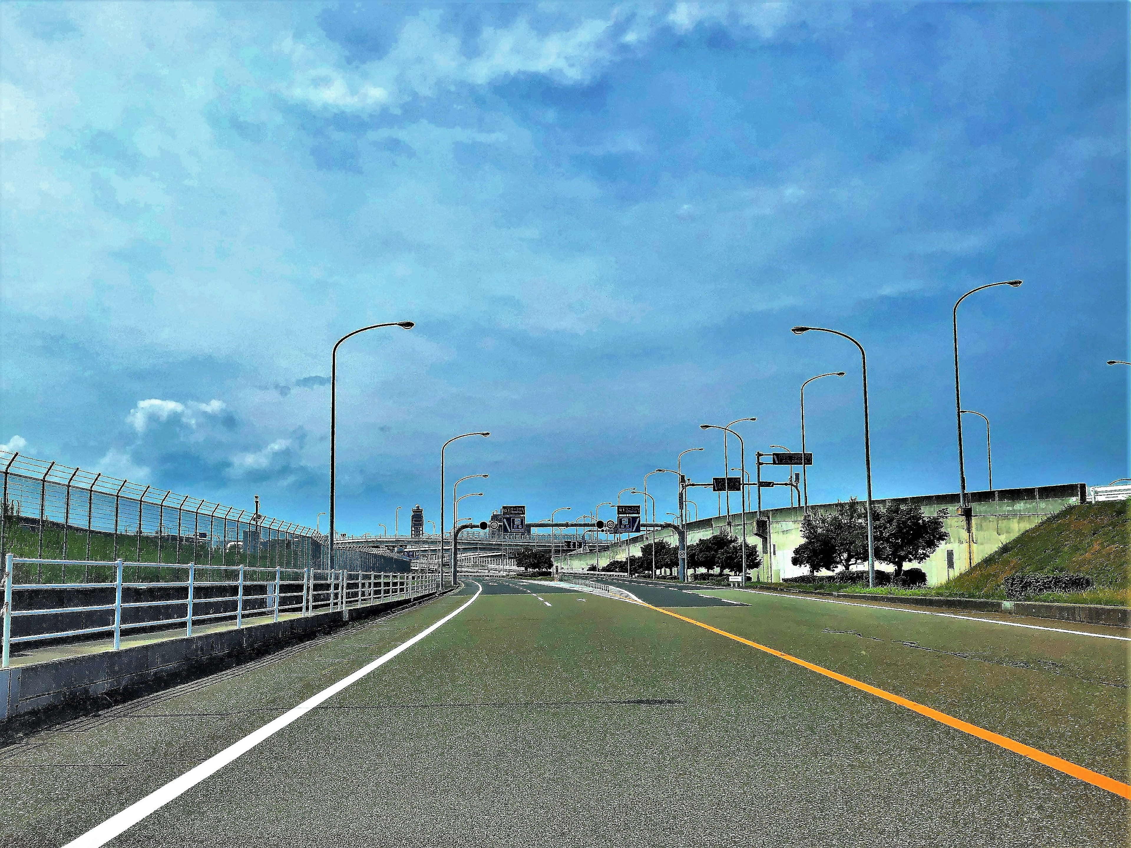 A wide road under a blue sky with streetlights