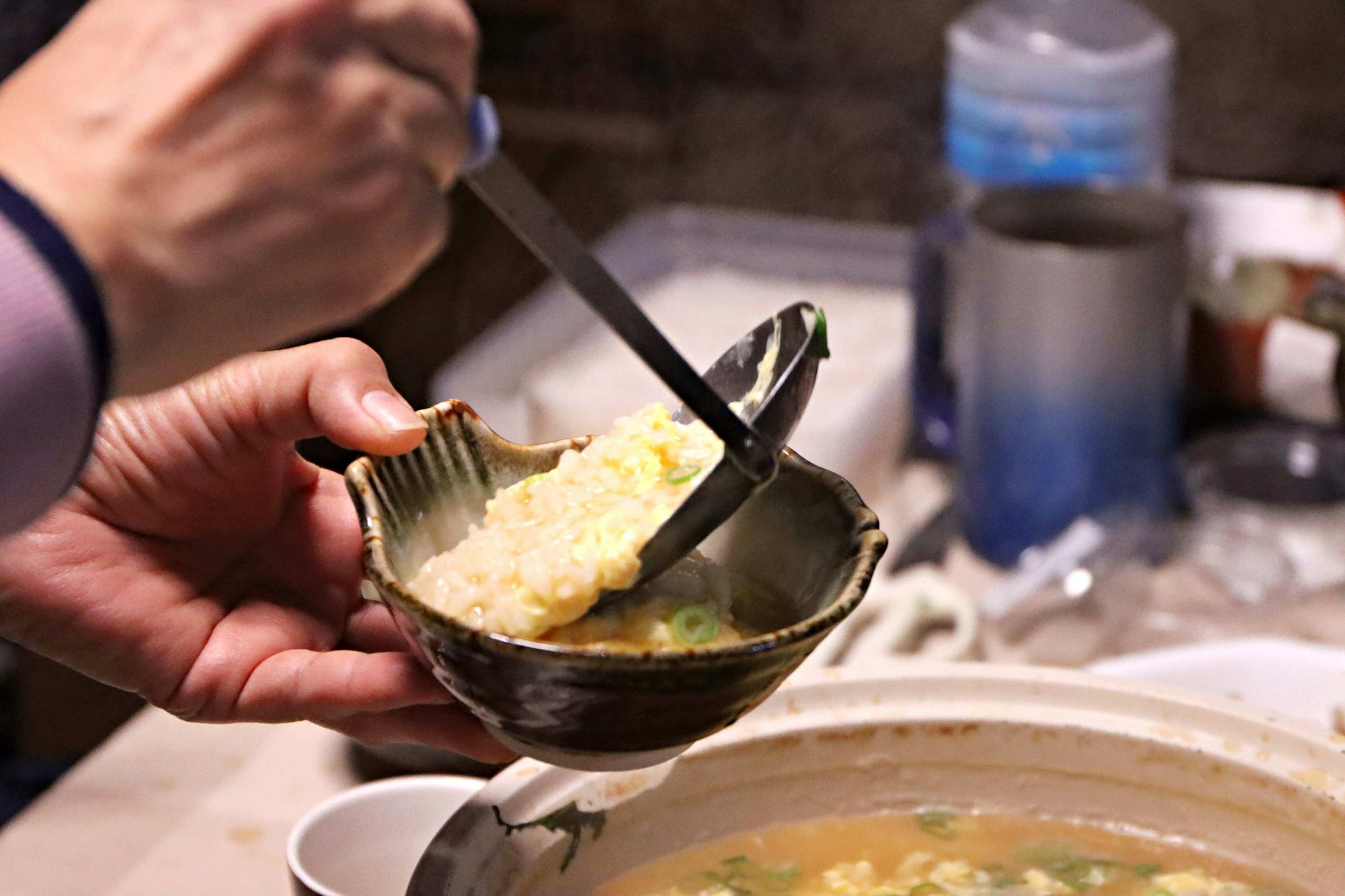 Person using a spoon to scoop soup into a bowl