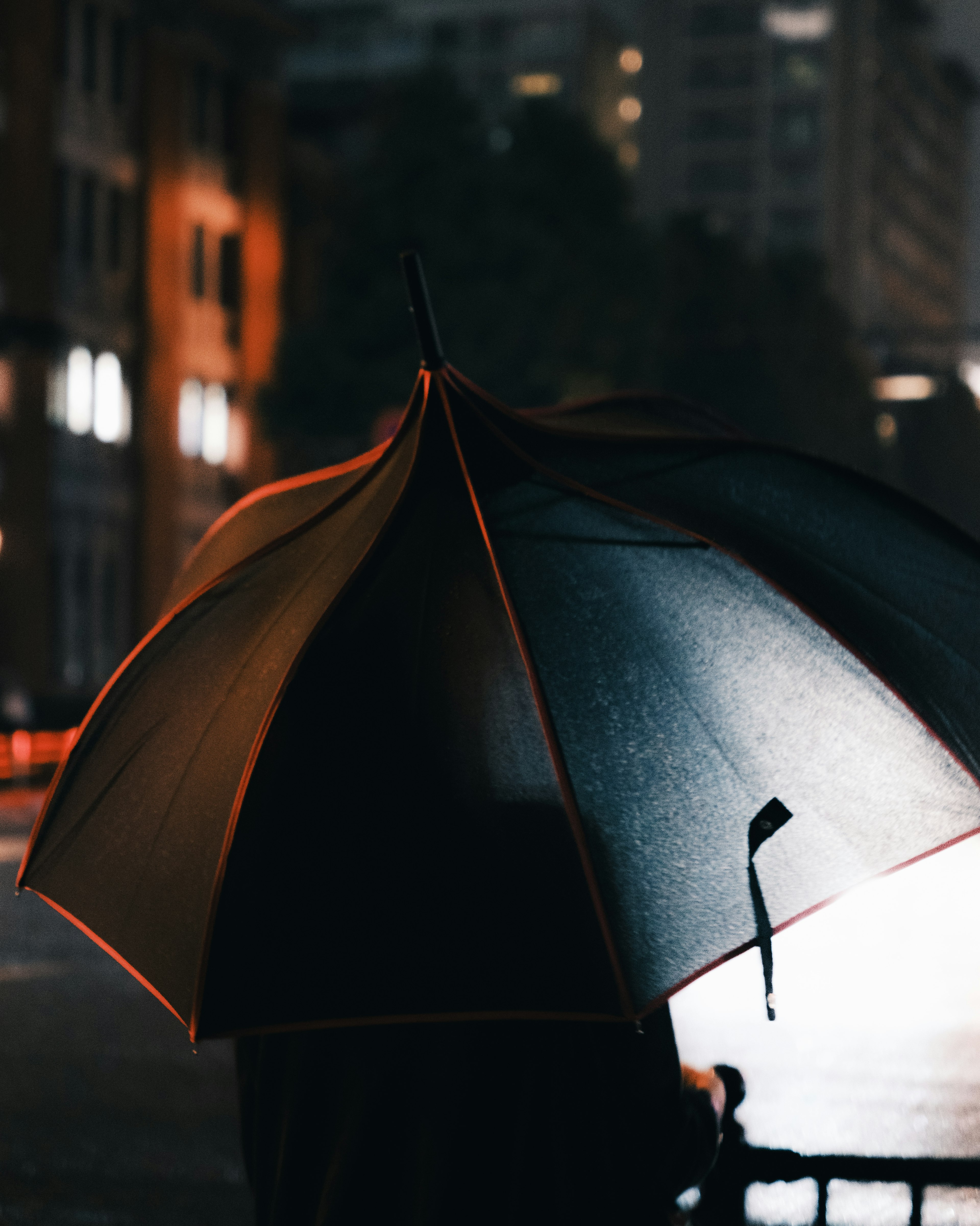 Eine Szene mit einer Person, die einen Regenschirm in einer Stadt bei Nacht hält