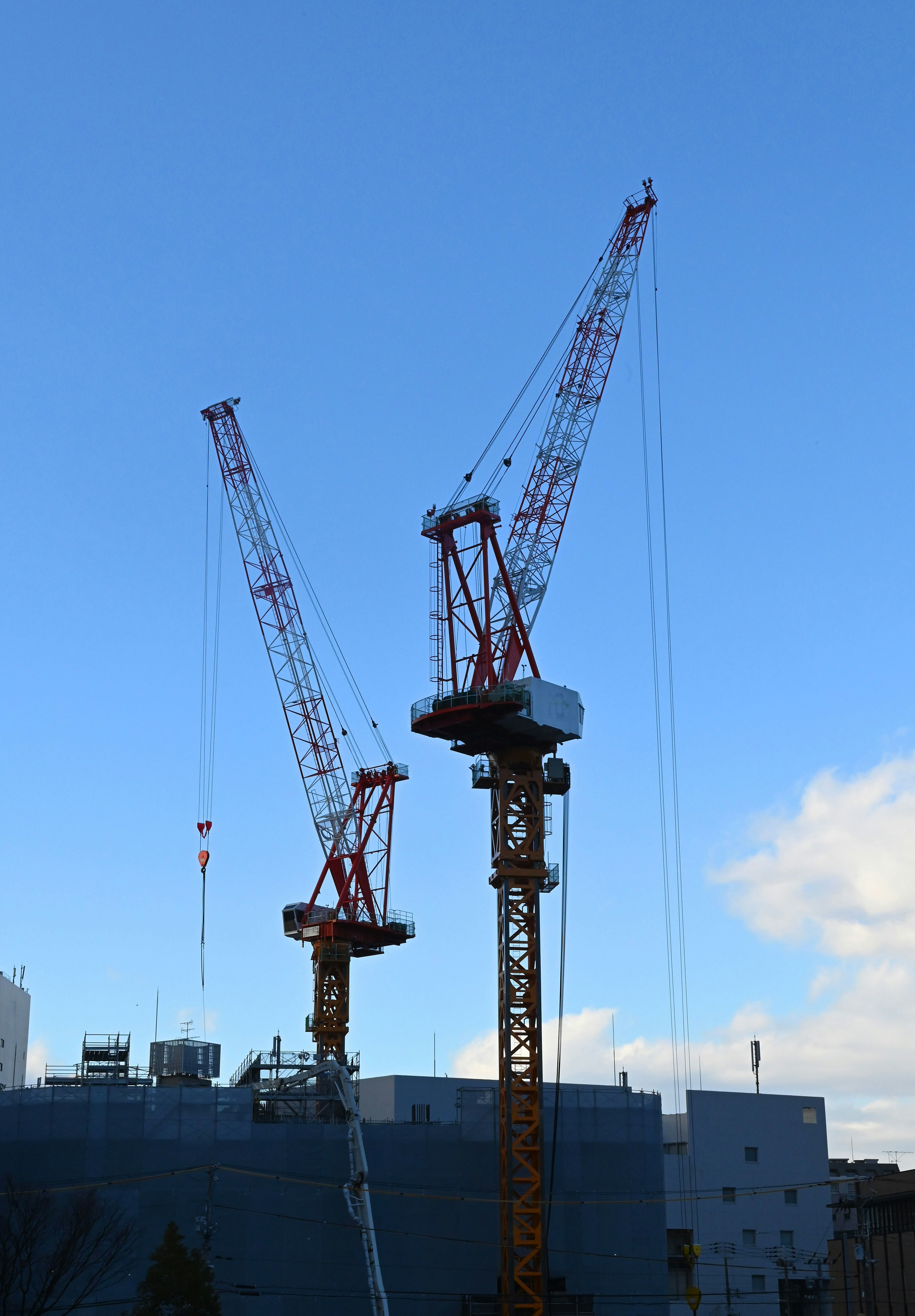 Two cranes working at a construction site under a blue sky