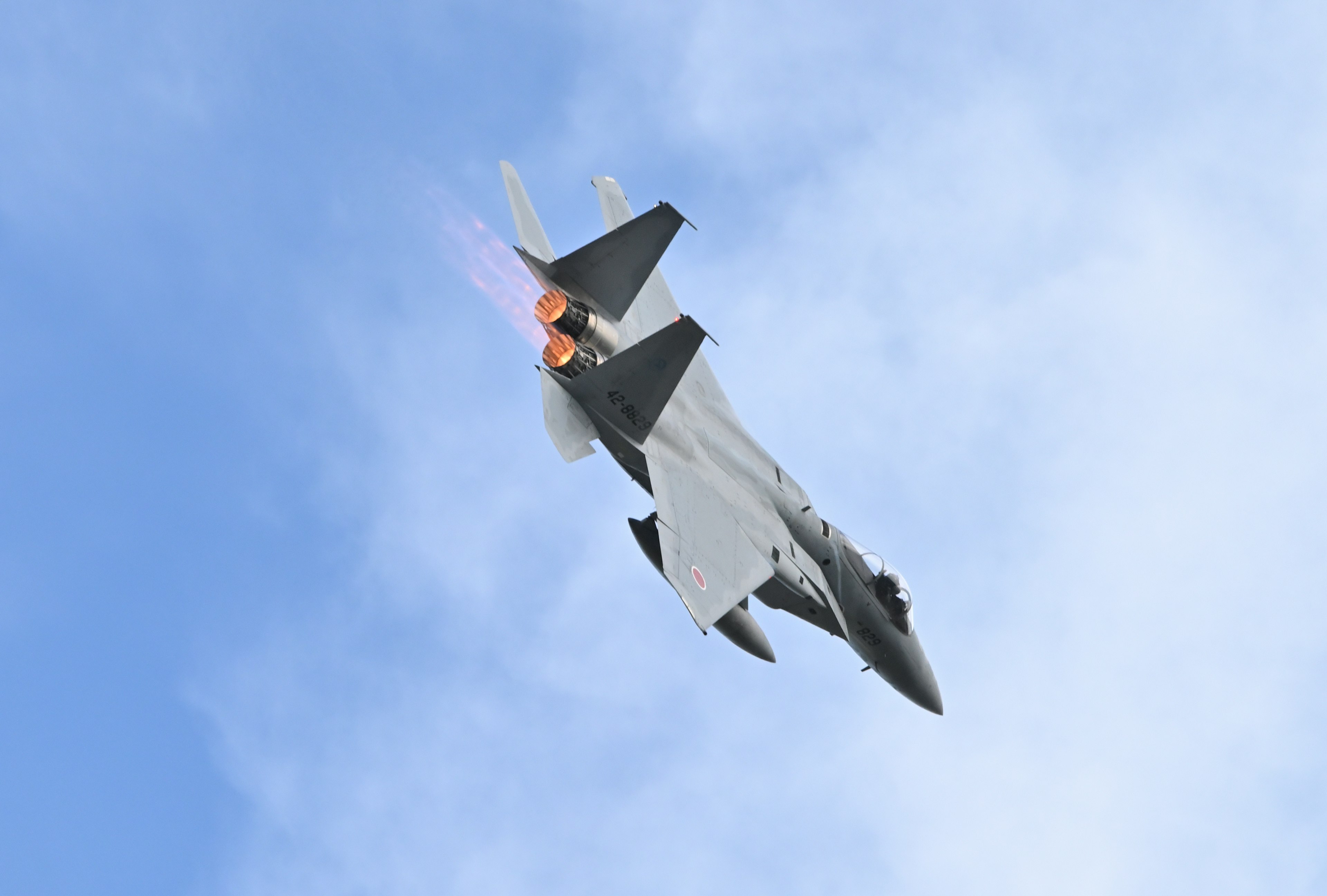 A fighter jet performing a maneuver in the sky with engine flames and smoke visible